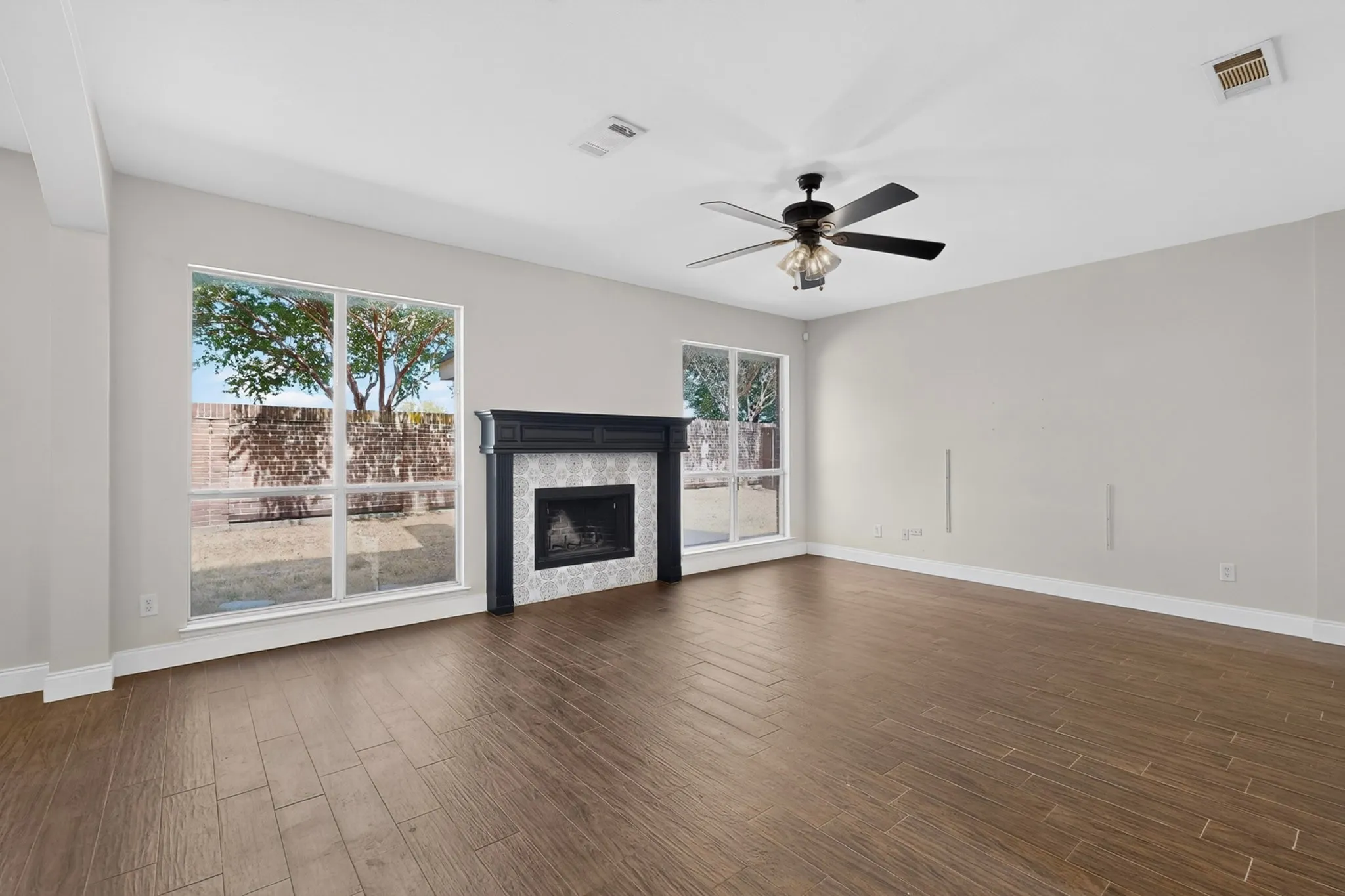 Spacious living area featuring wood-finish flooring, a decorative fireplace with a tile surround, and multiple windows