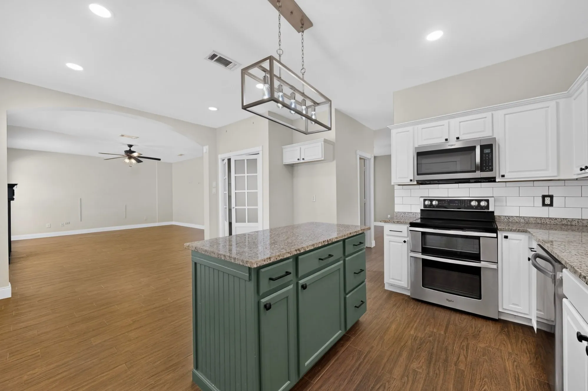 Kitchen island with stone-finish countertop, white cabinetry, stainless steel appliances, and wood-finish flooring