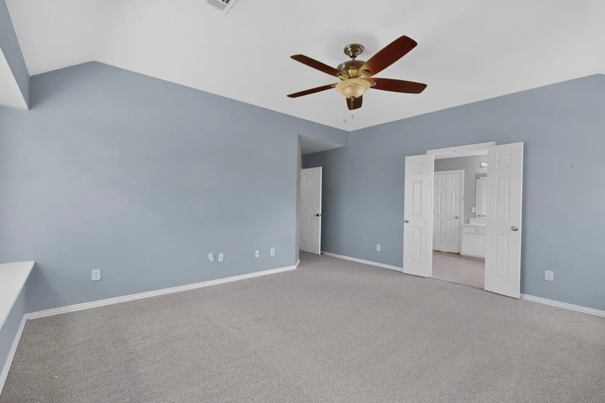 Vaulted ceiling, ceiling fan, neutral carpet, double doors, and a built-in shelf