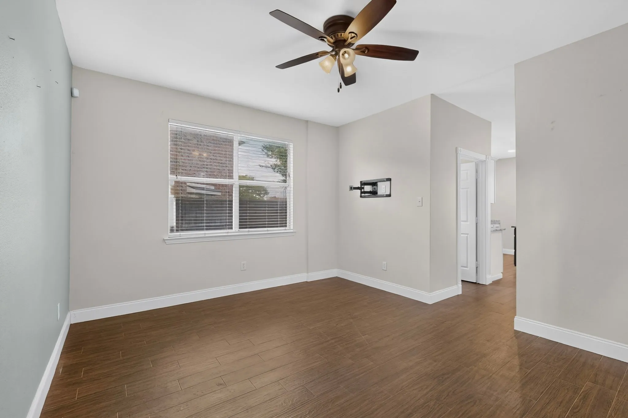 Wood-finish flooring, ceiling fan with integrated lighting, window with blinds, and light neutral wall colors