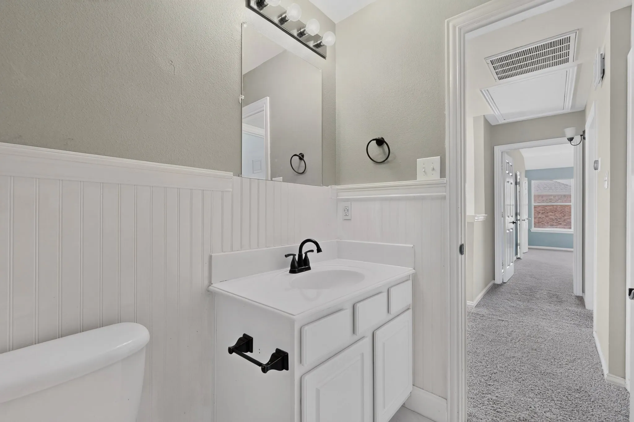 Bathroom vanity with white cabinetry, black faucet, and beadboard wainscoting