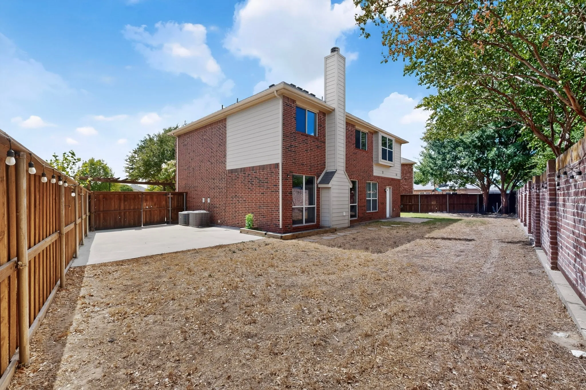 Rear exterior with brick and siding facade, featuring a concrete patio and a wood privacy fence