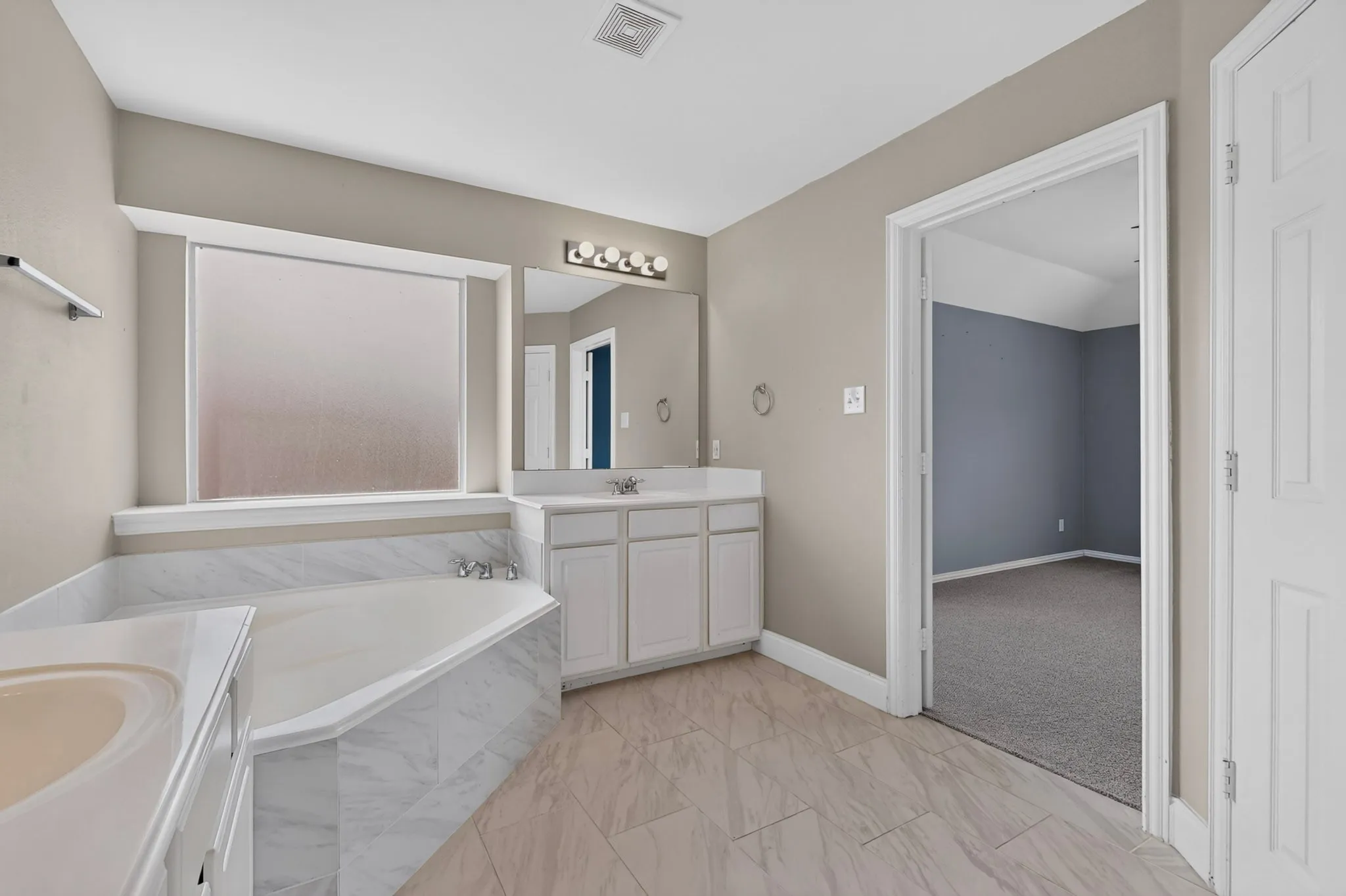 Dual vanity with white cabinetry, a built-in corner soaking tub, a large privacy window, and wood-finish flooring