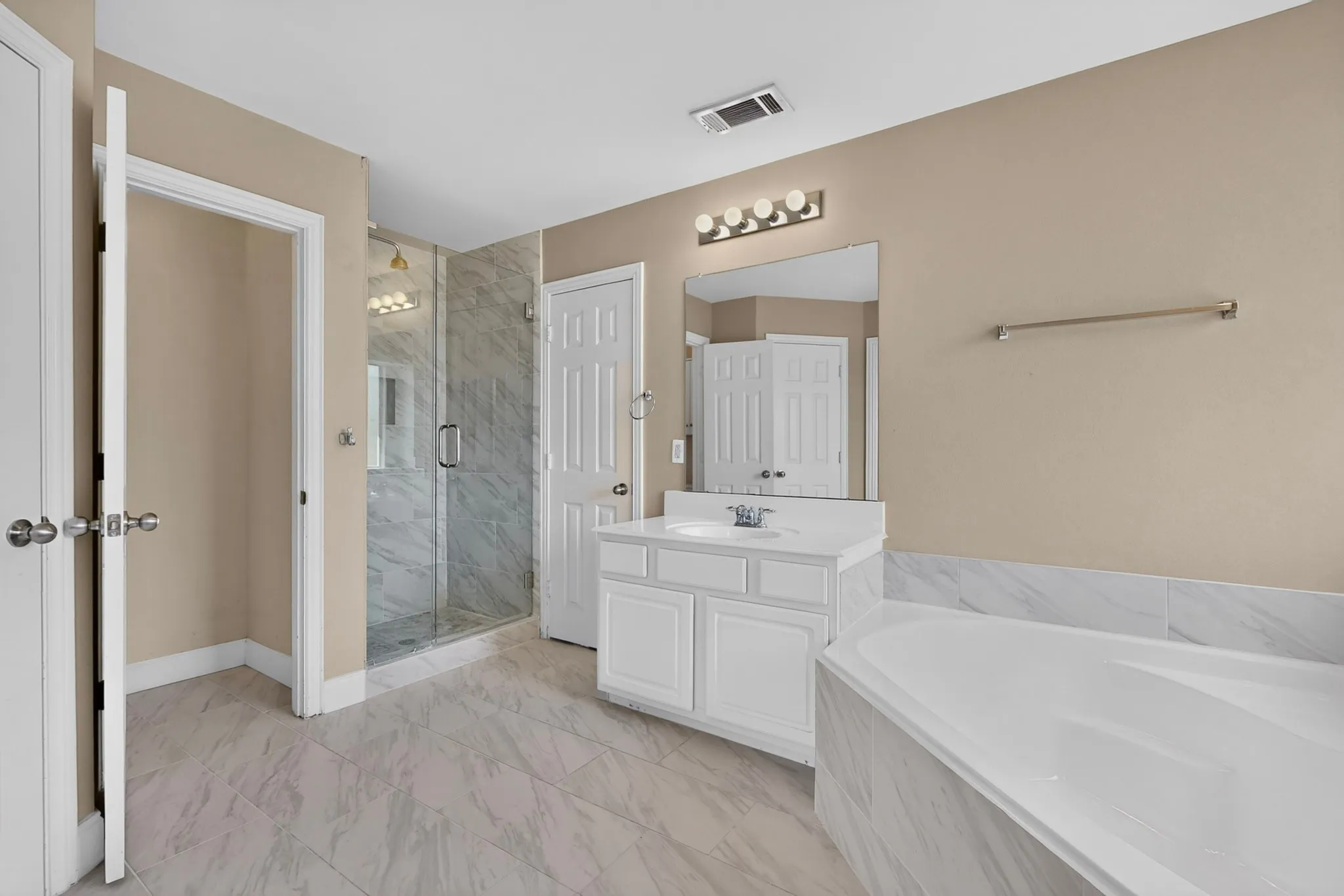 Spacious bathroom featuring a glass-enclosed shower, a separate built-in soaking tub, a single vanity with a white countertop, and tiled flooring