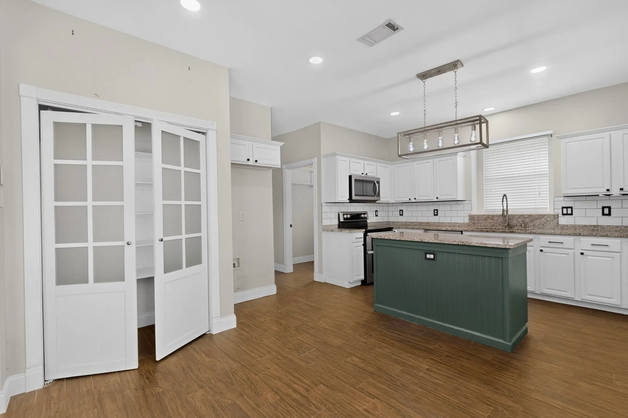 Kitchen featuring a central island, wood-finish flooring, white cabinetry, integrated appliances, and a tiled backsplash