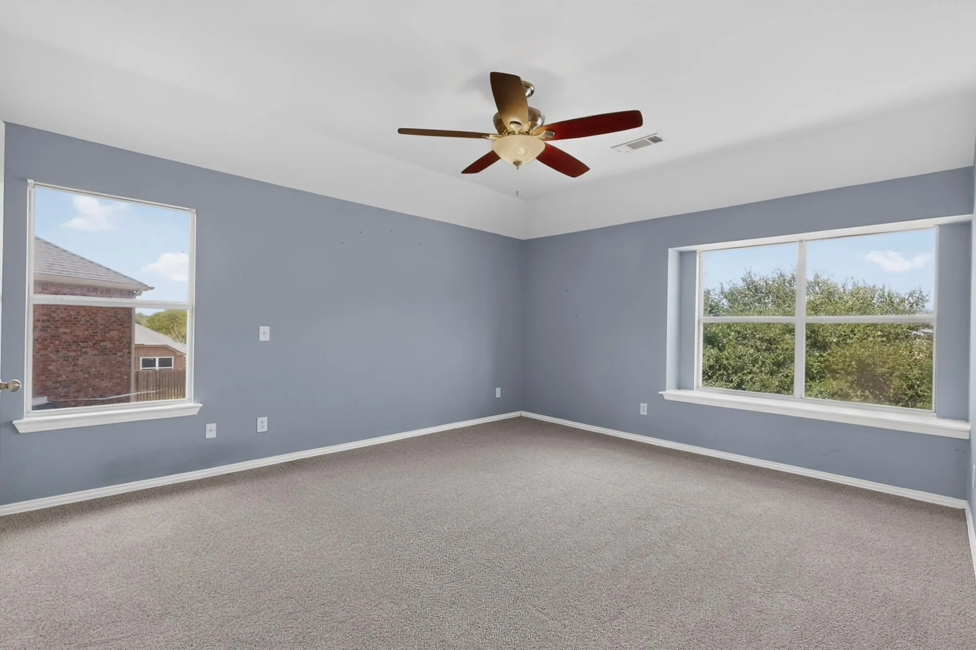 Spacious room featuring two large windows, a ceiling fan with integrated lighting, recessed ceiling details, and neutral carpeting