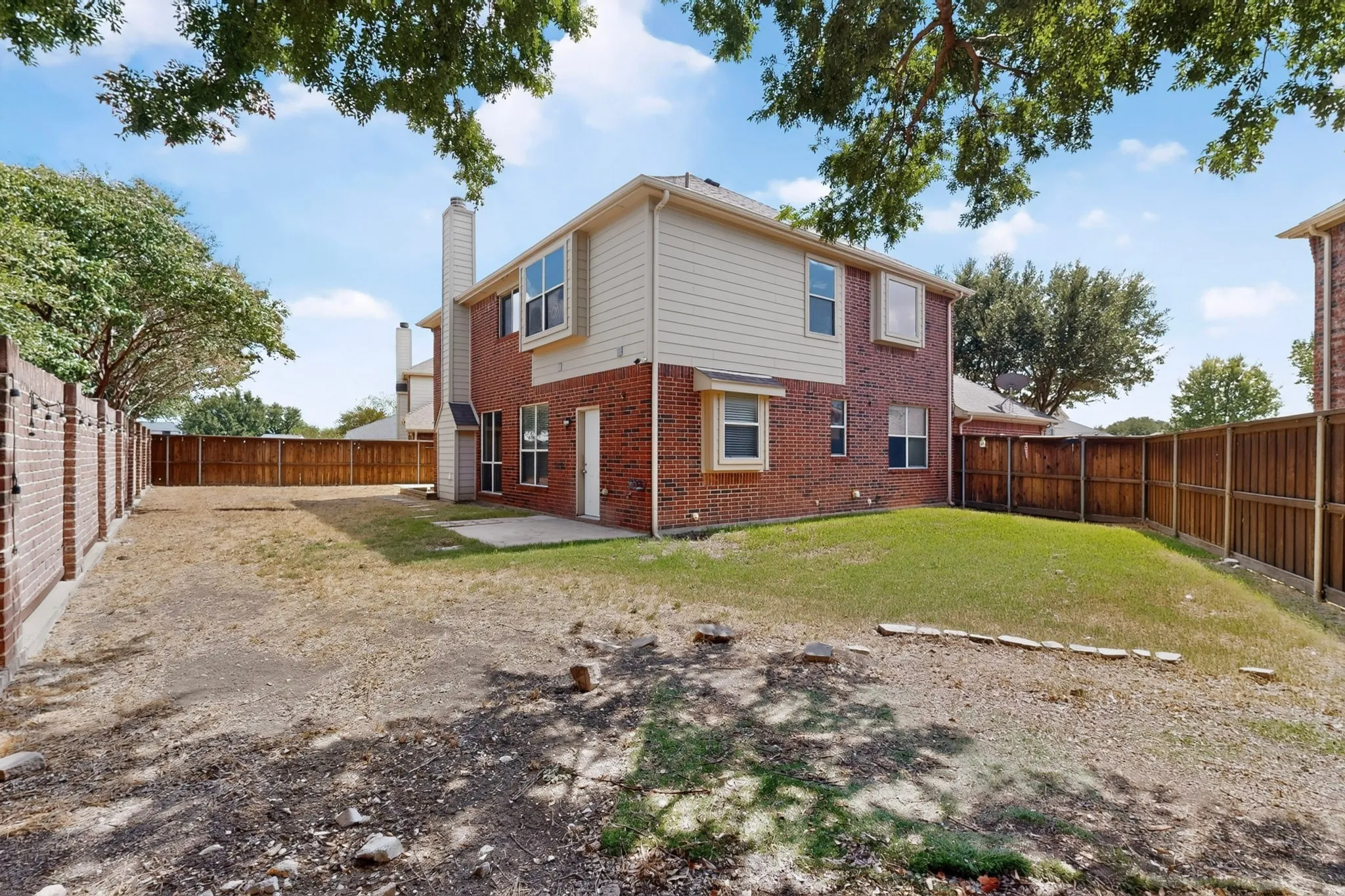 Expansive backyard featuring a brick and siding exterior, privacy fencing, and a concrete patio