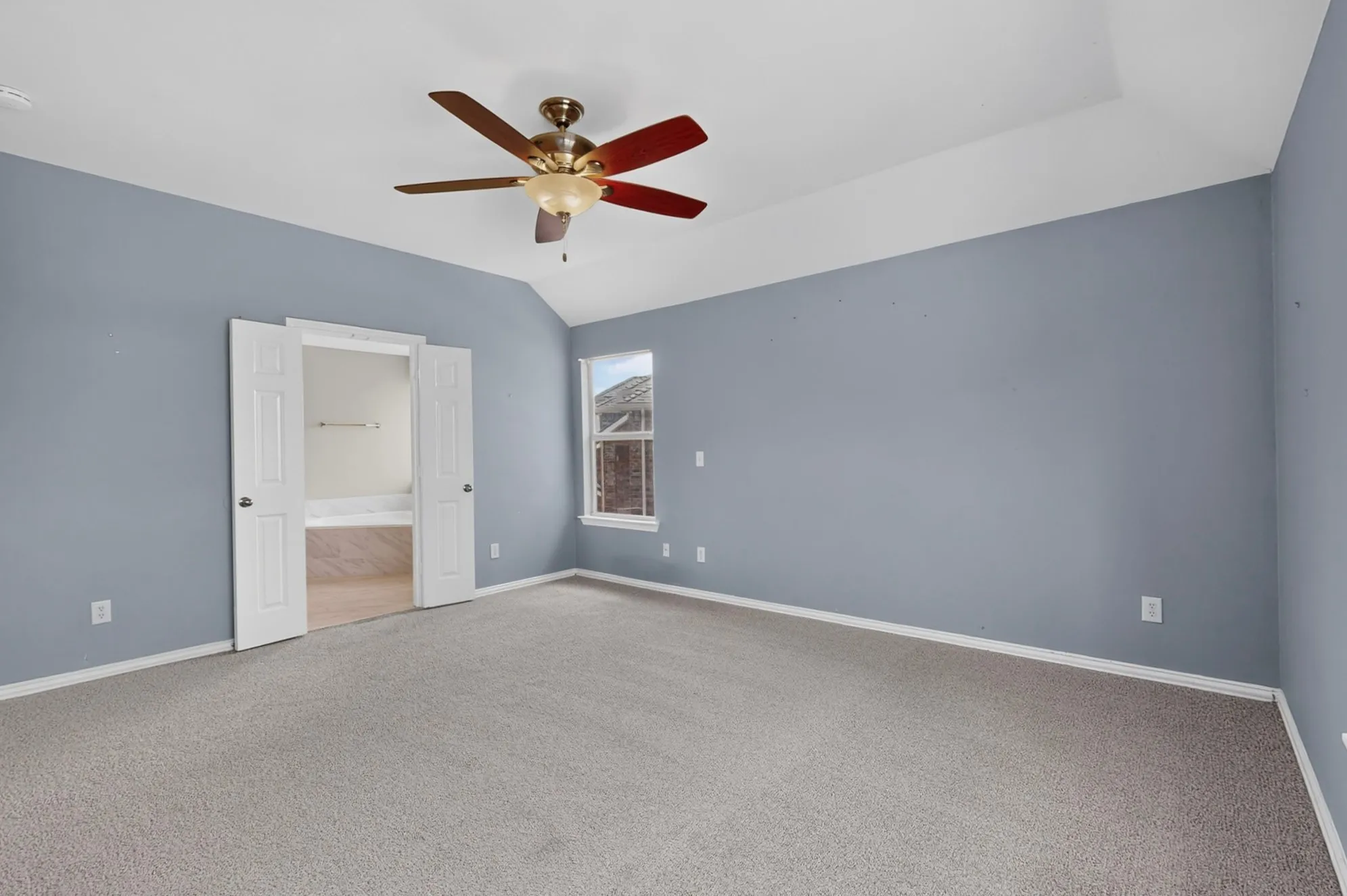 Vaulted ceiling with a ceiling fan, carpet flooring, window with exterior brick detail, and double panel interior doors