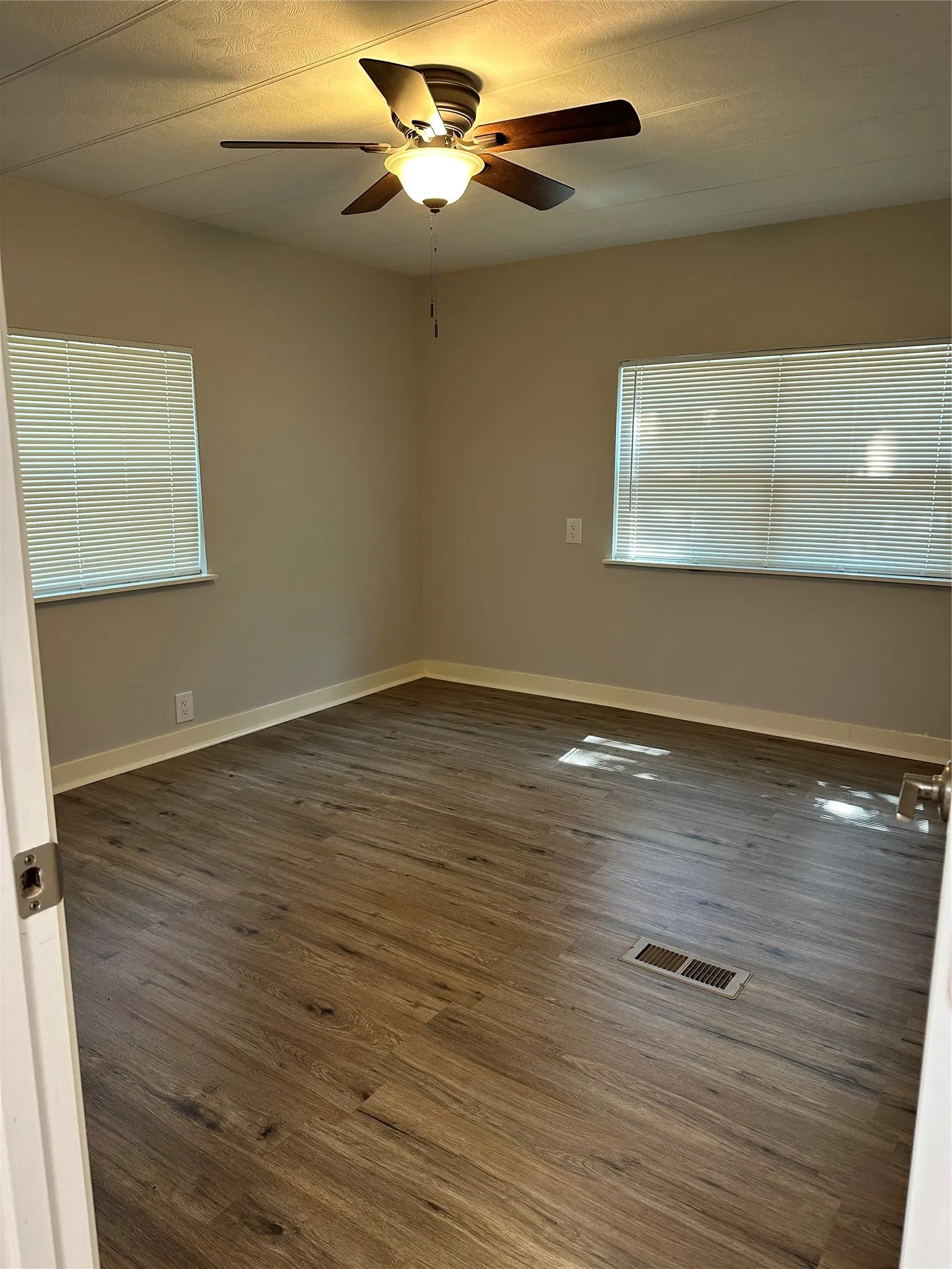 Empty room featuring dark wood-type flooring, plenty of natural light, and a ceiling fan
