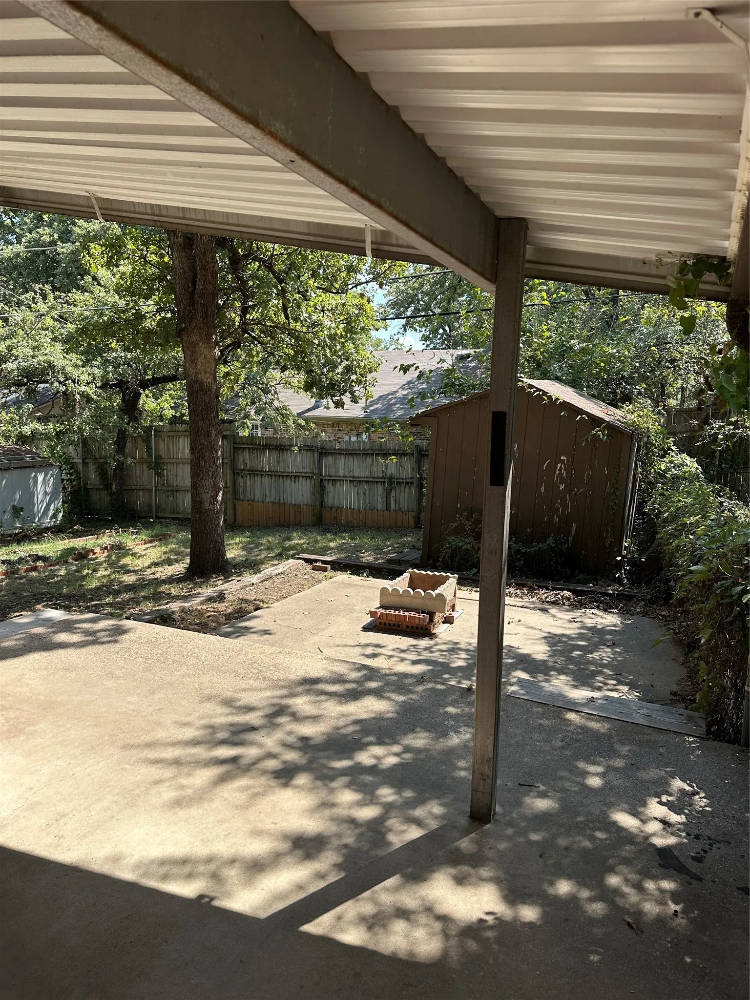 View of backyard from large covered back patio area and wooden privacy fence.