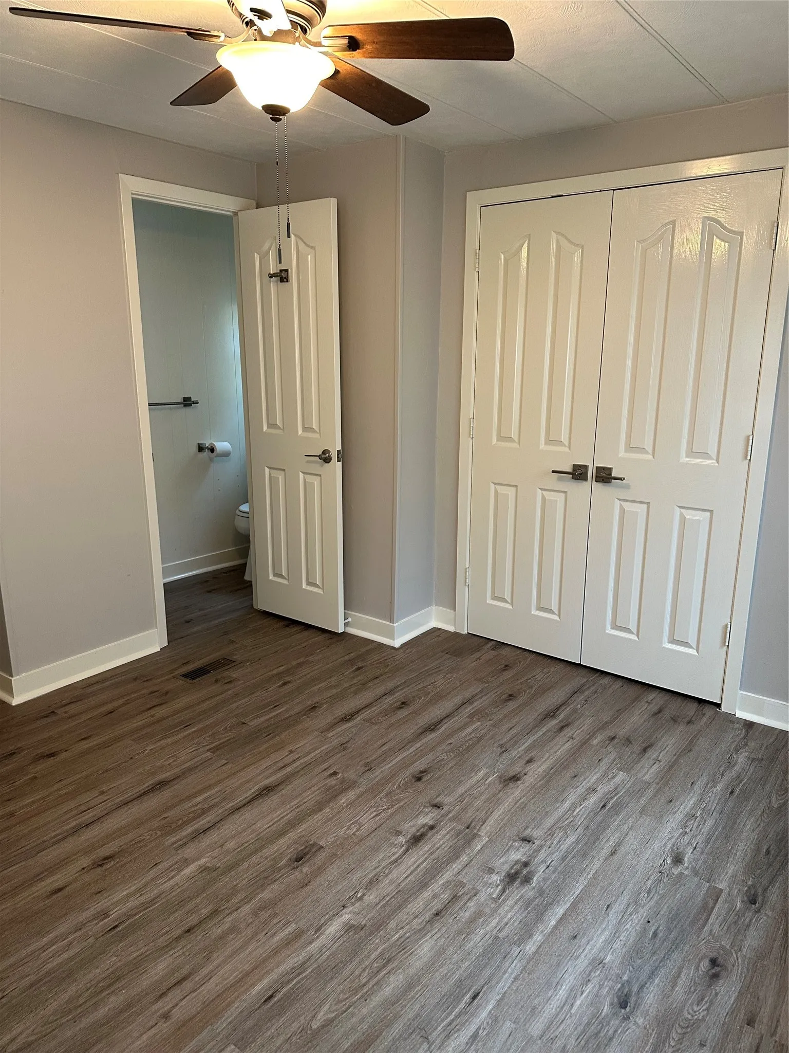 Unfurnished bedroom with dark wood-style floors, a ceiling fan, a closet, and connected bathroom