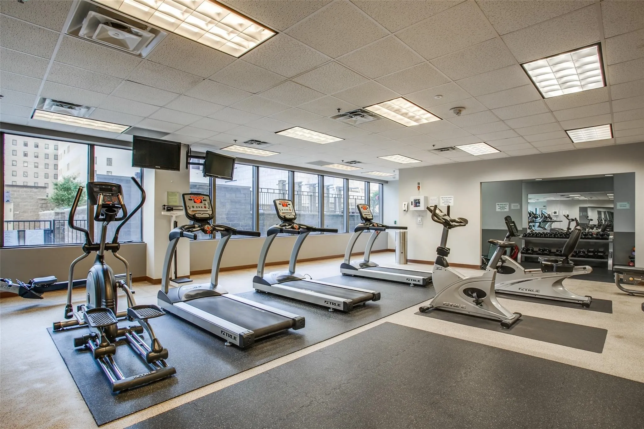 Dedicated fitness room with multiple exercise machines, mirrored wall, and recessed lighting