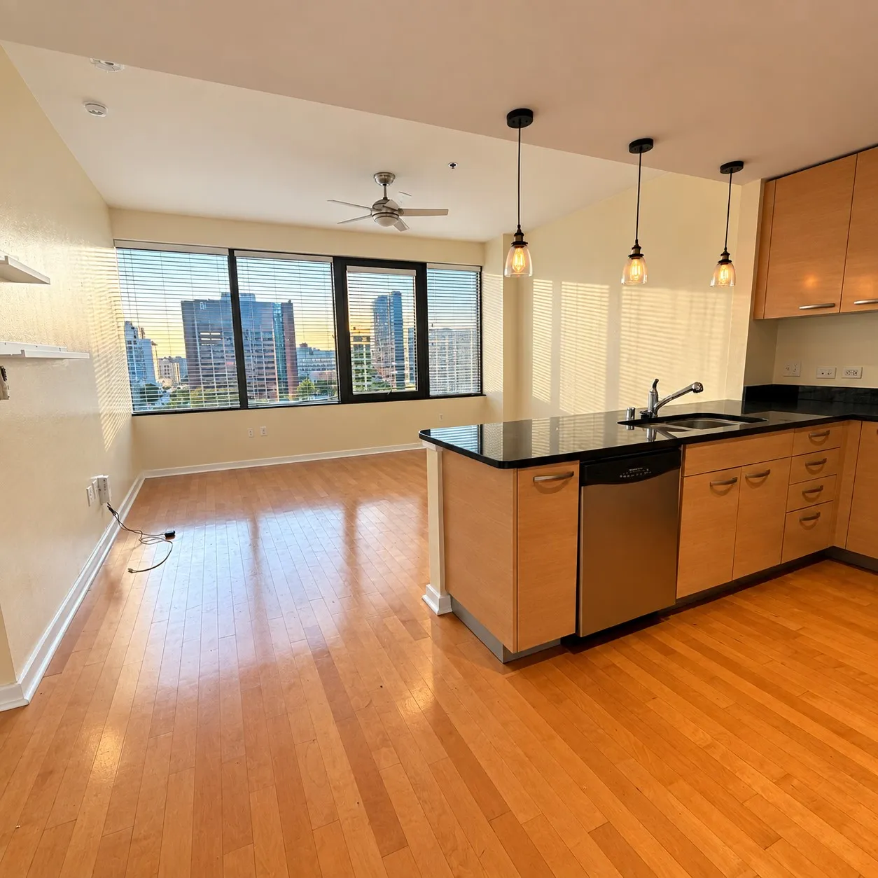 Open-concept living space with expansive windows, wood-finish flooring, a ceiling fan, and a kitchen island with a dark countertop and stainless steel appliances