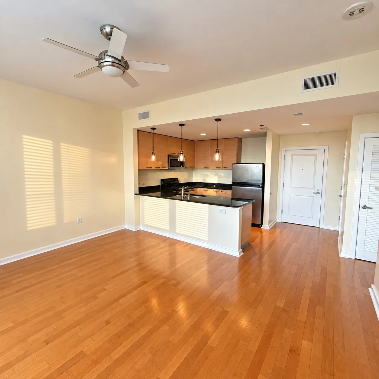 Hardwood flooring throughout, kitchen with dark countertops, wood-finish cabinetry, stainless steel appliances, and a ceiling fan with integrated lighting