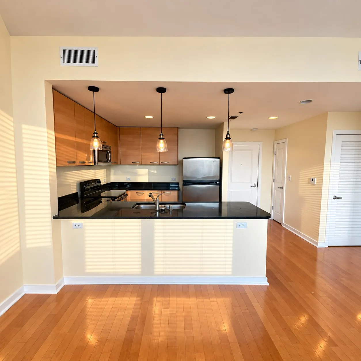 Open-concept kitchen featuring wood cabinetry, dark countertops, stainless steel appliances, and a breakfast bar with pendant lighting