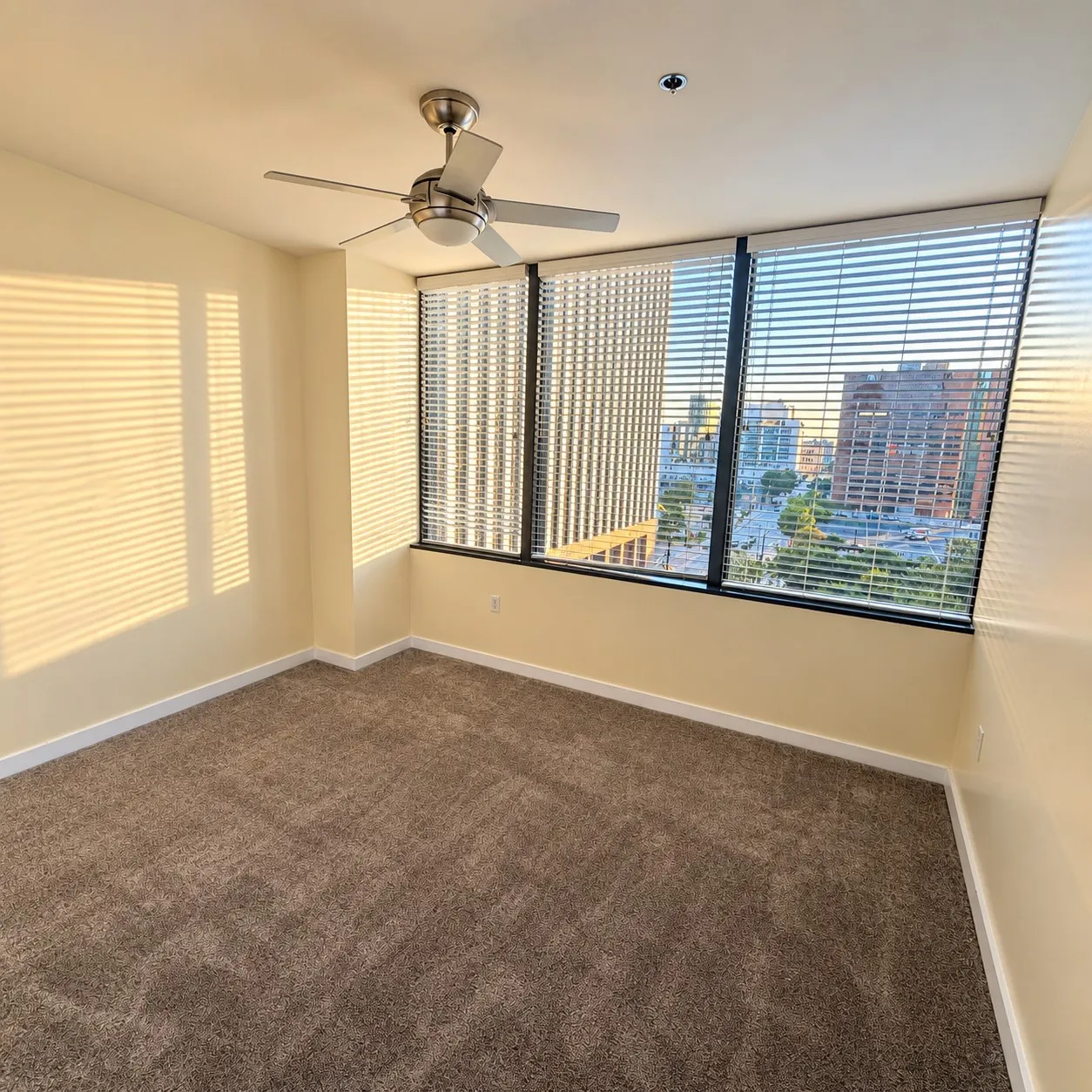 Expansive window wall with horizontal blinds, neutral tone carpeting, ceiling fan with integrated lighting, and recessed ceiling lighting
