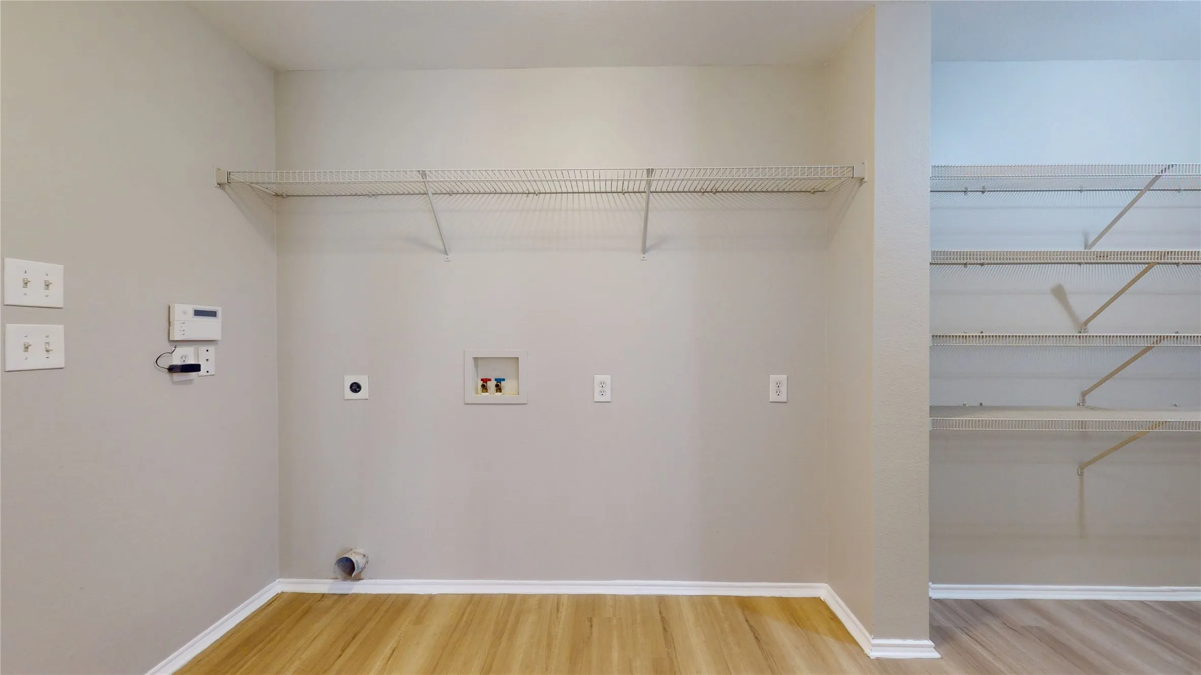 Wood-finish flooring with white baseboards, wire shelving, and utility hookups
