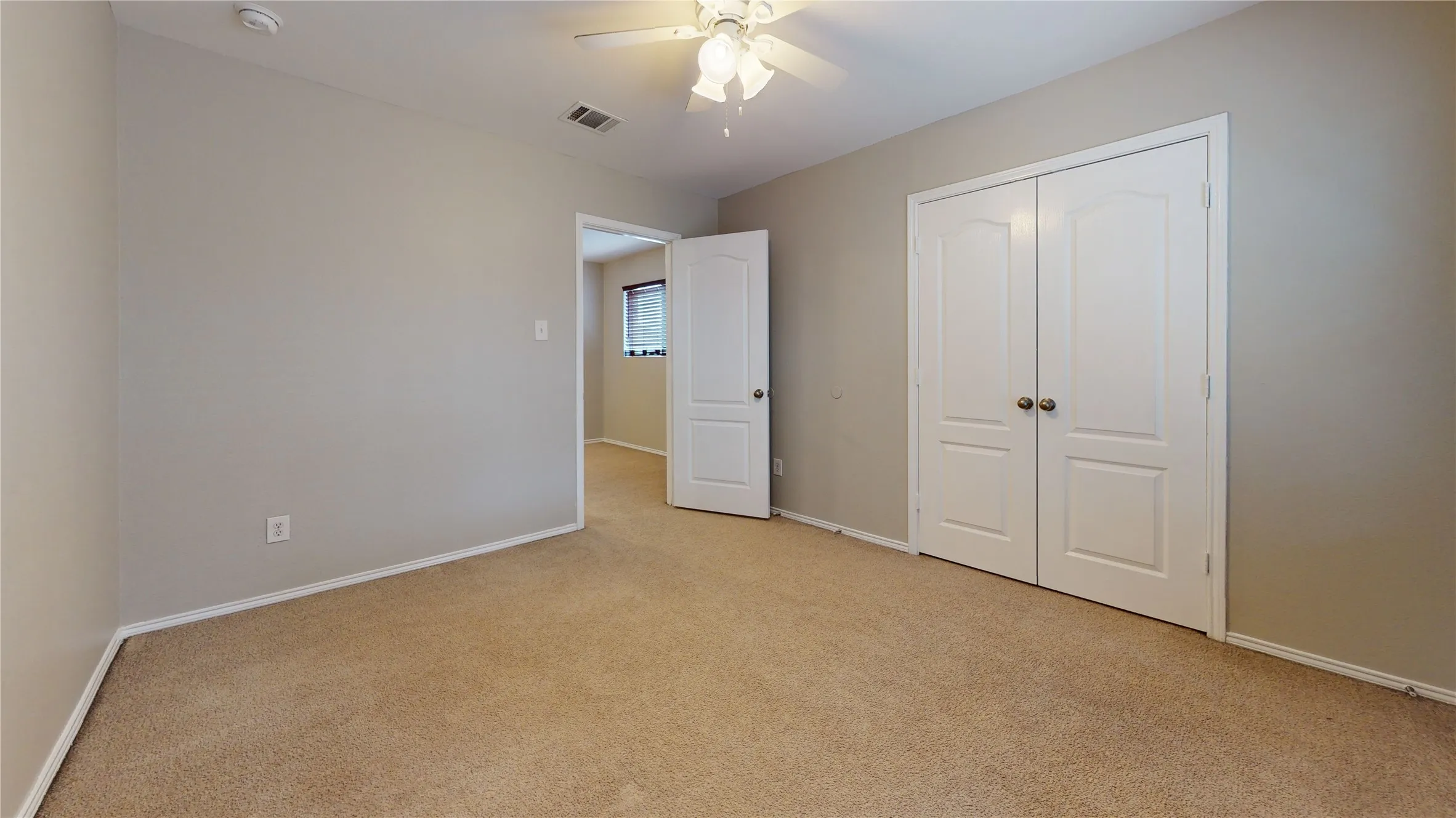 Neutral tone walls with light carpeting, white double-panel doors, and a ceiling fan