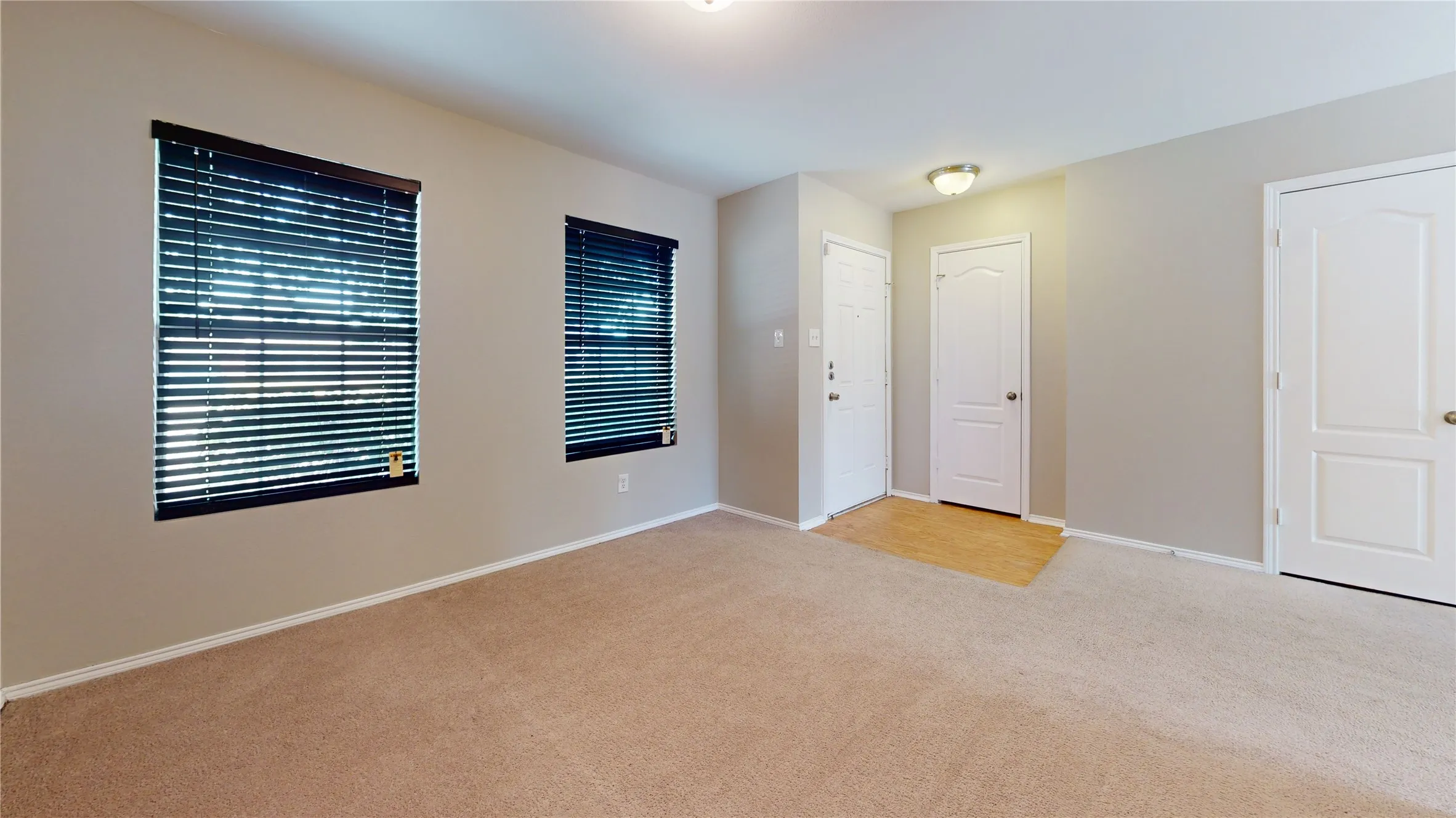 Carpeted room with neutral wall tones and two windows featuring horizontal blinds