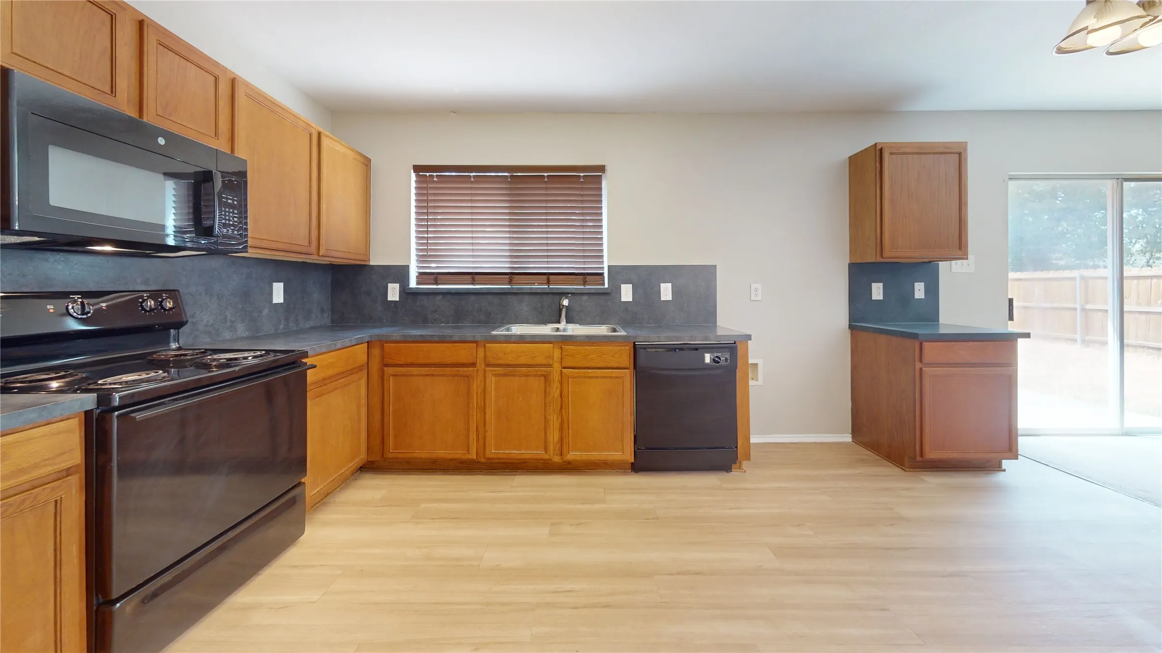 Wood-finish flooring, wood cabinetry, black appliances, solid surface countertops, and sliding glass door