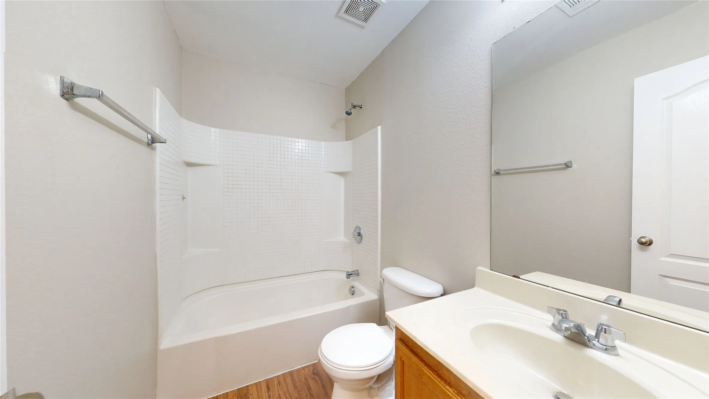 Bathroom featuring a combination shower and tub with tile surround, wood-finish flooring, a vanity with an integrated sink, and a large wall mirror
