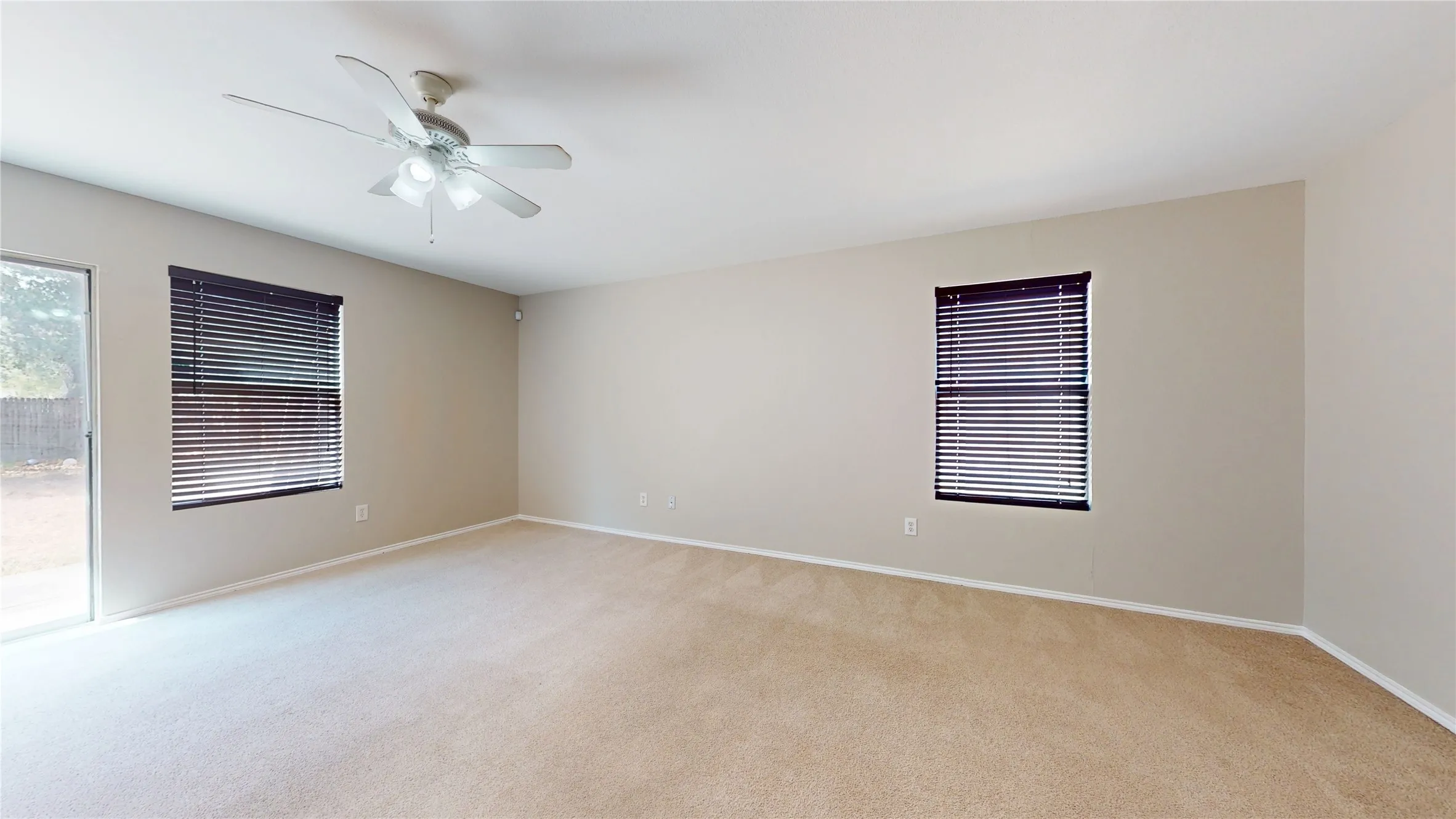Neutral wall paint, carpet flooring, a ceiling fan with light fixture, and multiple windows with blinds