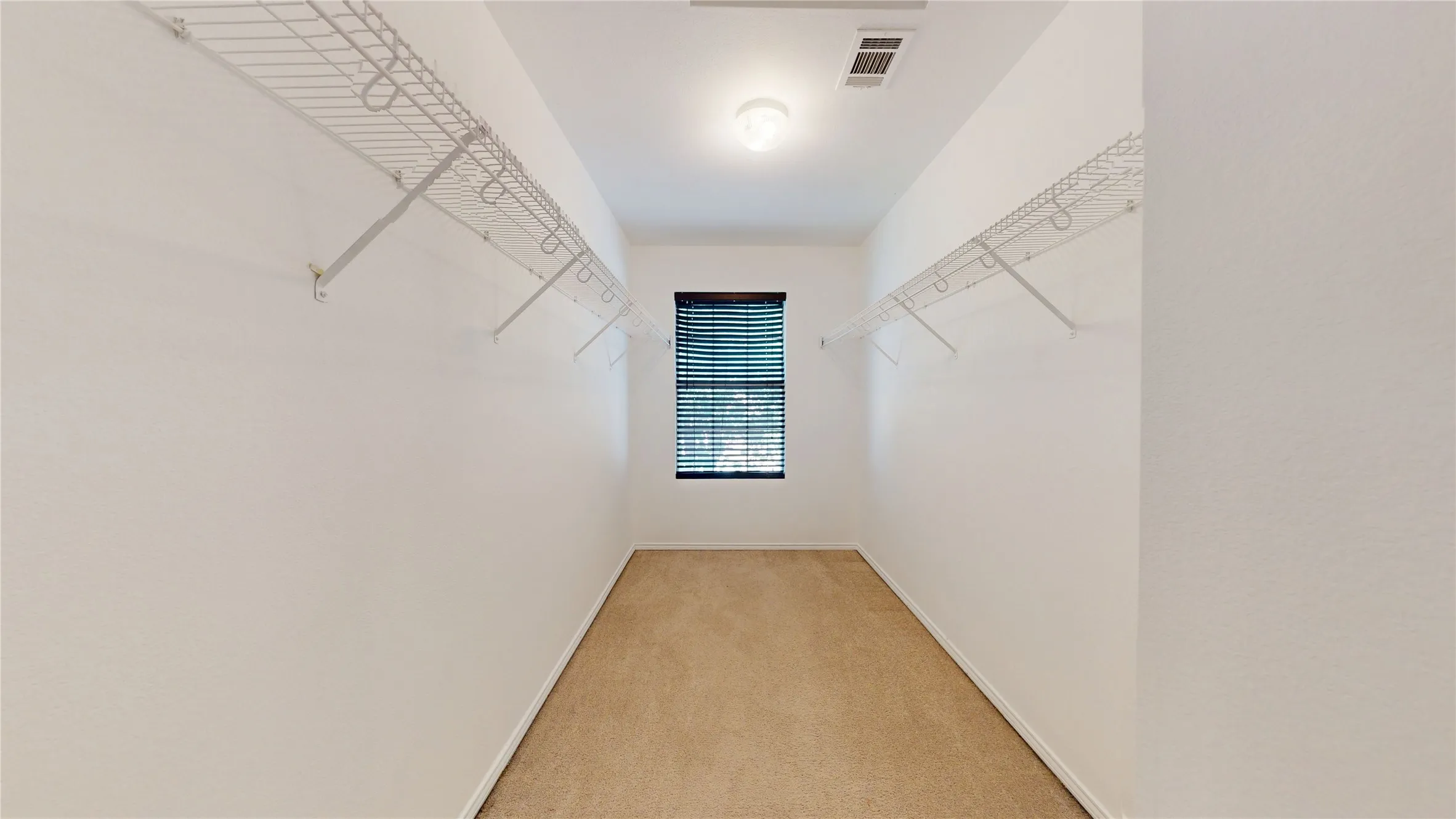 Recessed window with horizontal blinds, overhead ceiling light, wire shelving system, and carpet flooring
