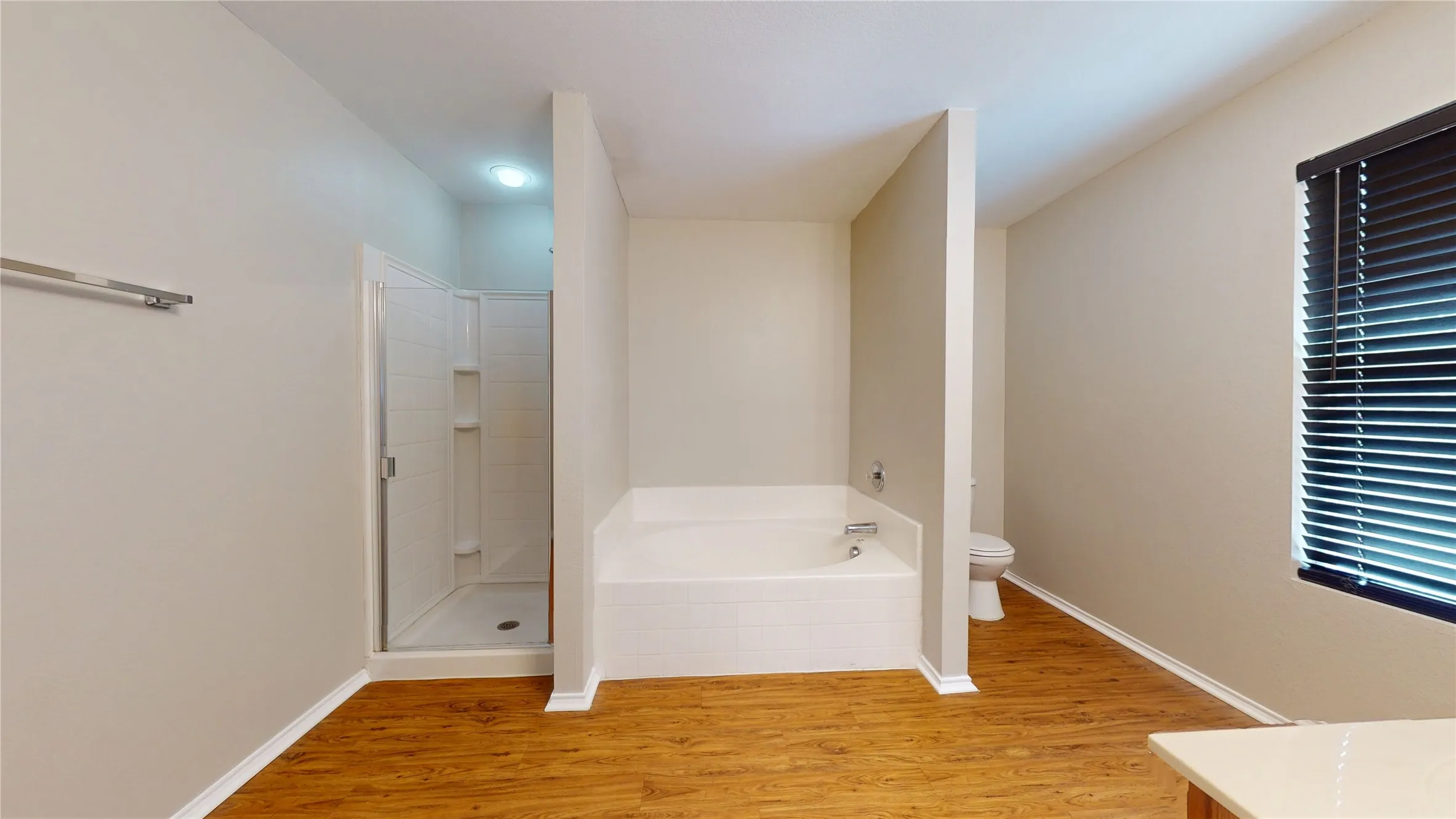 Enclosed shower with glass panel, white built-in bathtub, and wood-finish flooring