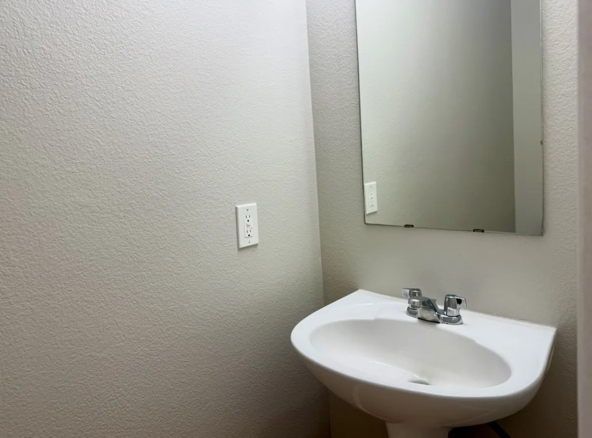 Pedestal sink with a chrome faucet and a wall-mounted rectangular mirror