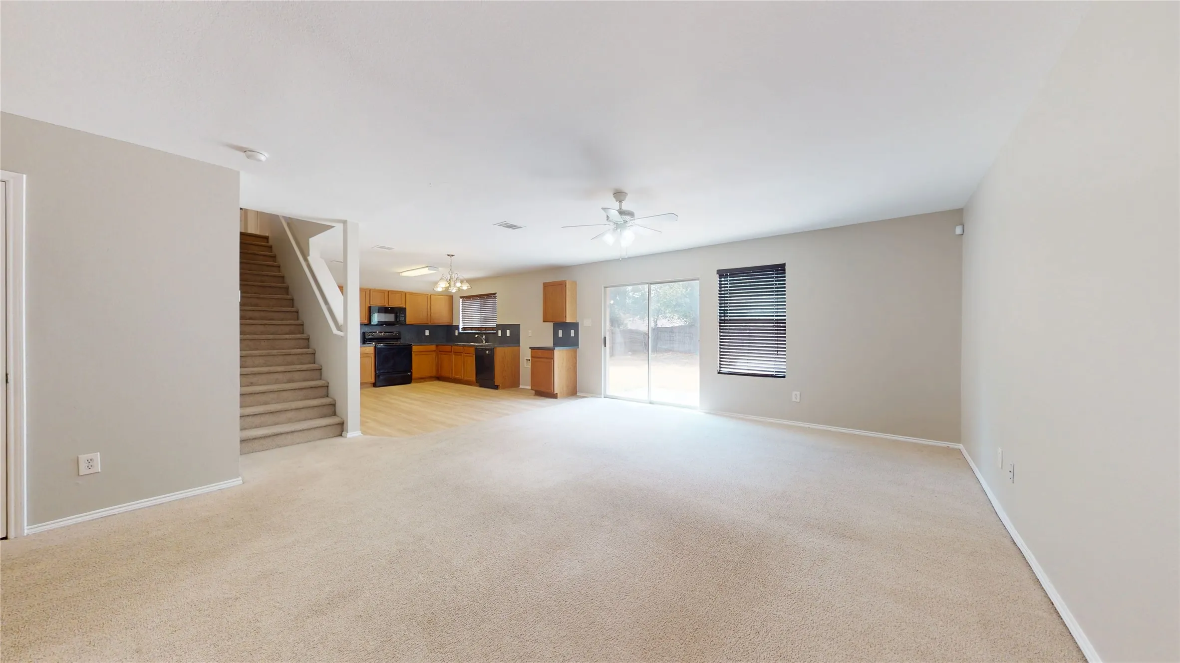 Open-concept living space with light-toned walls, carpeted flooring, a ceiling fan, and a sliding glass door
