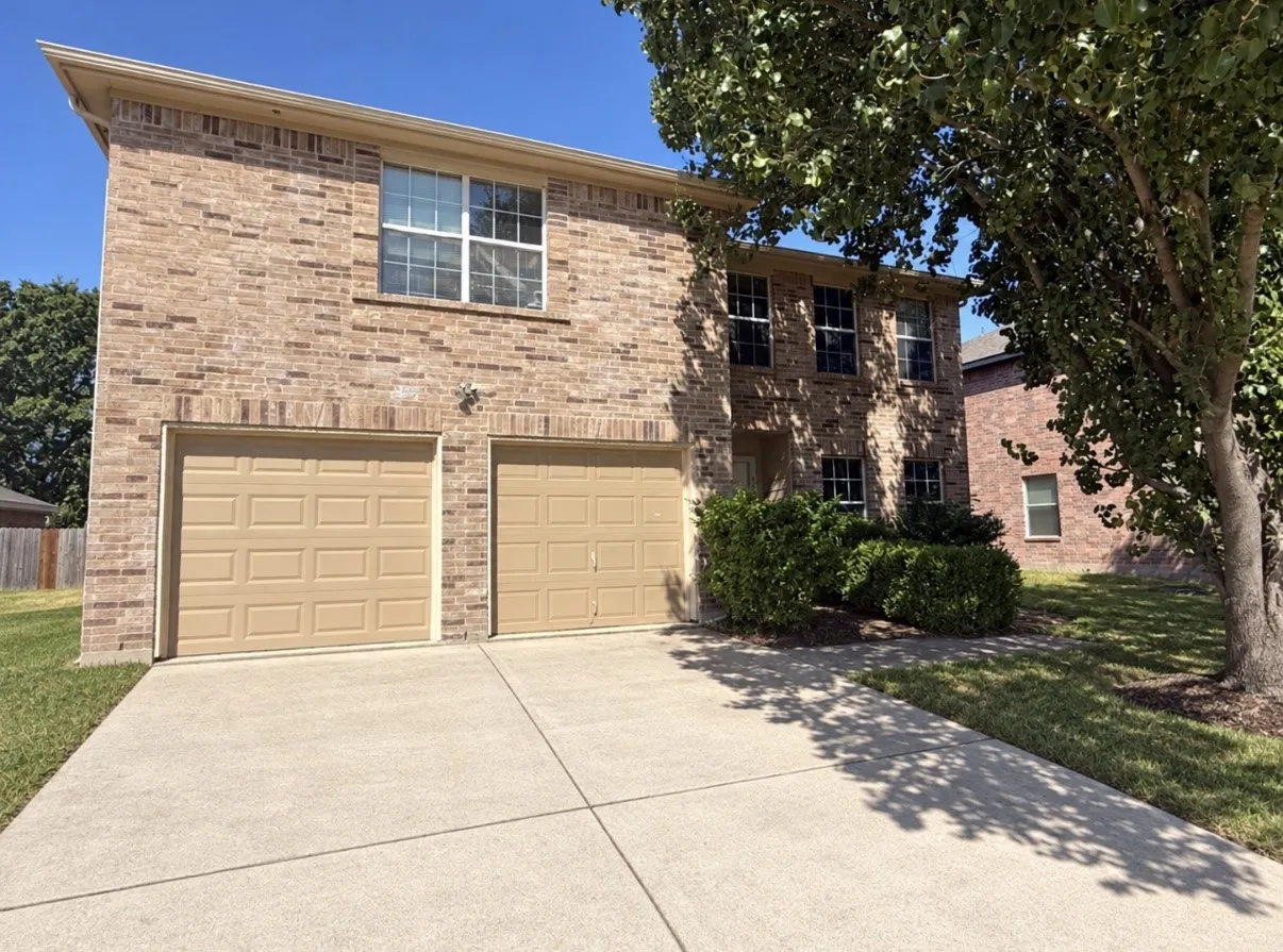 Brick exterior, two-car garage, concrete driveway, mature landscaping, and multiple windows