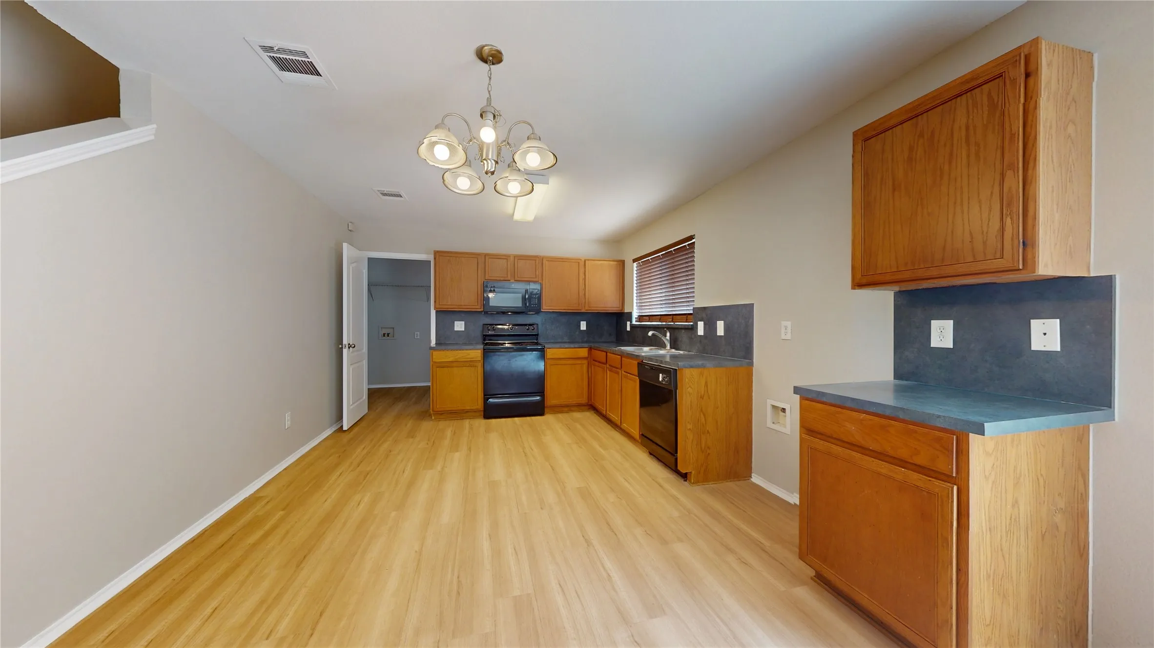 Open-concept kitchen with wood-finish flooring, ample wood cabinetry, dark countertops, and a full suite of black appliances