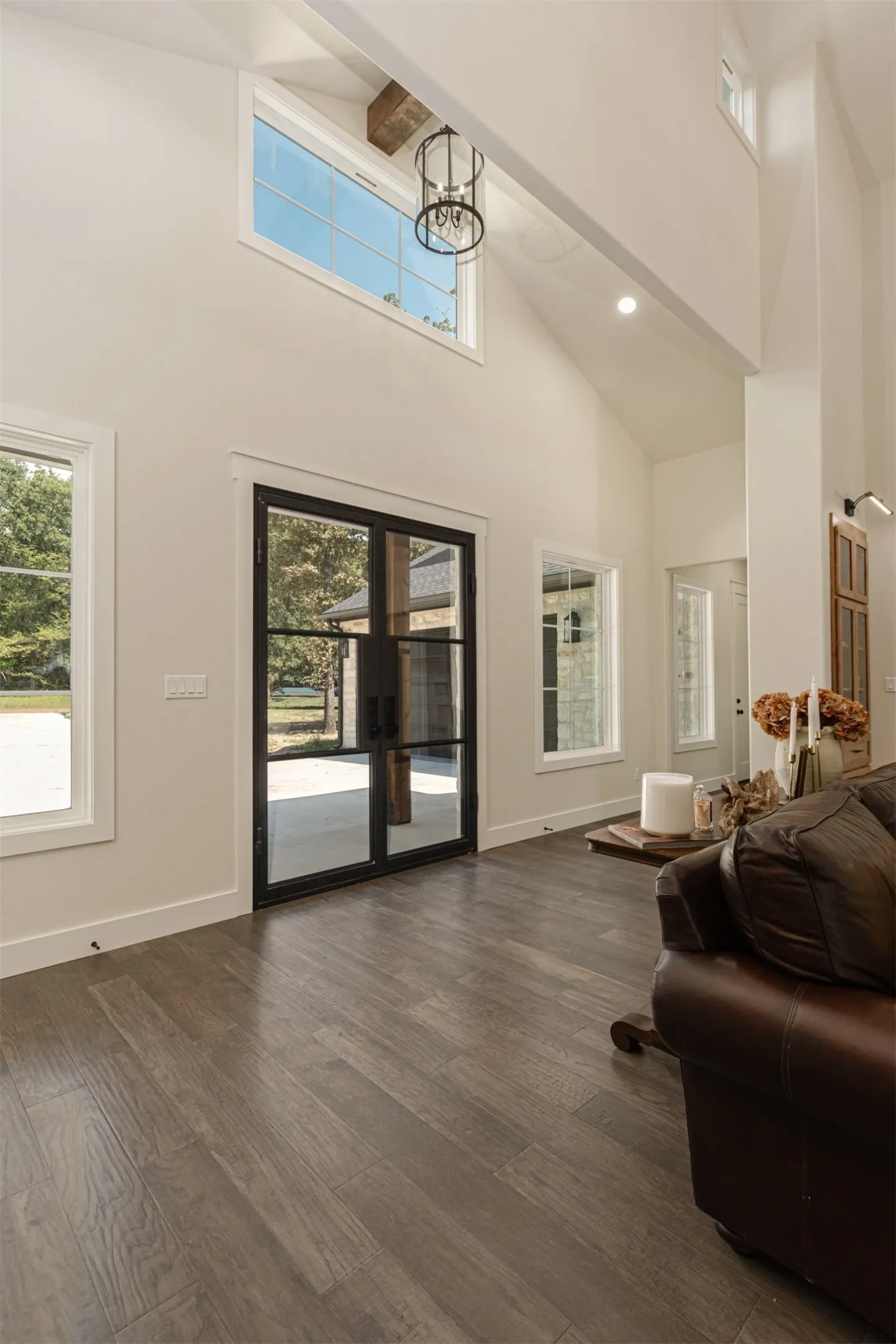 Vaulted ceiling with an exposed wood beam, wood-finish flooring, black-framed double entry doors, high transom windows, and recessed lighting