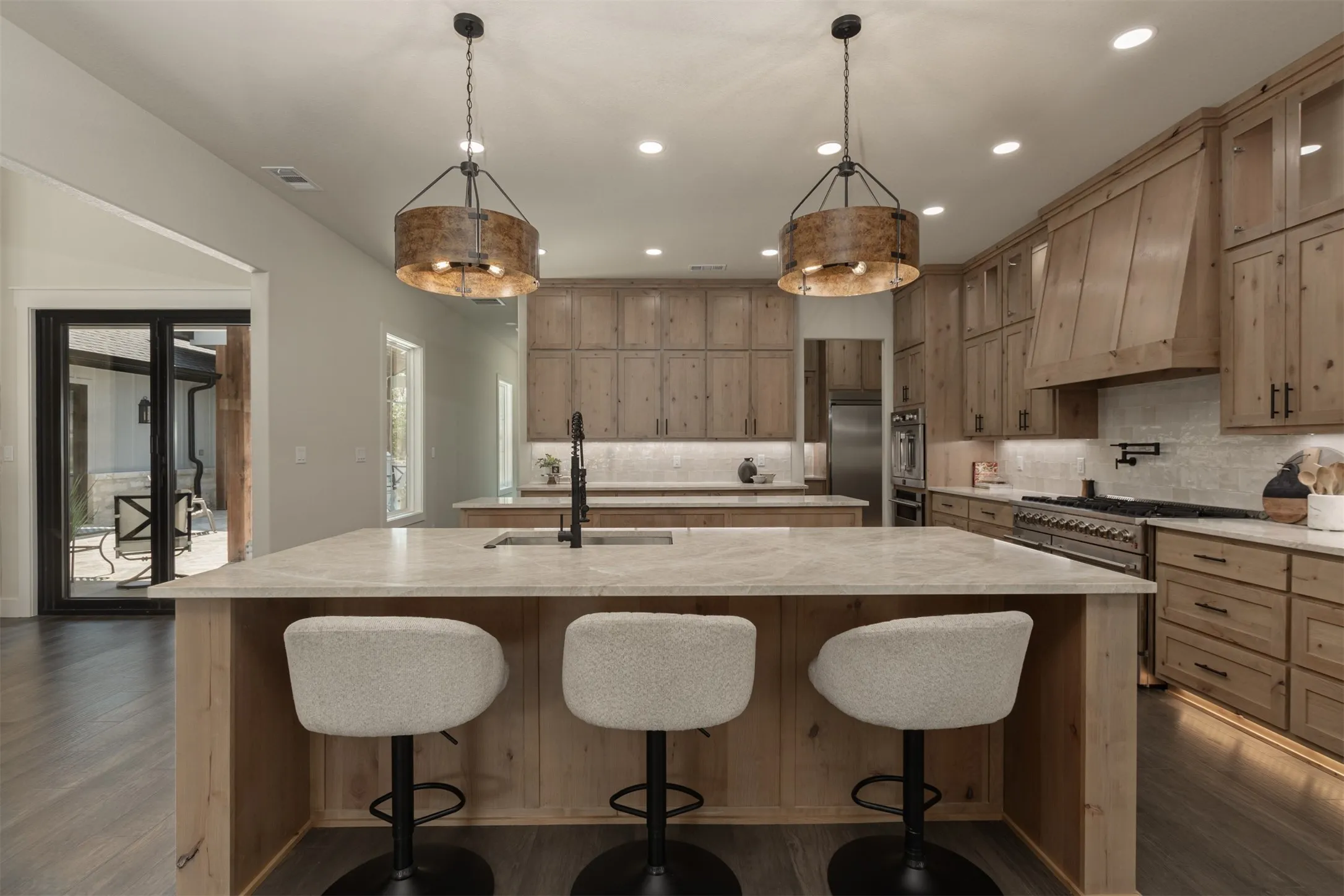Expansive kitchen island with light-toned countertop, wood-finish cabinetry throughout, stainless steel range with pot filler, and recessed lighting
