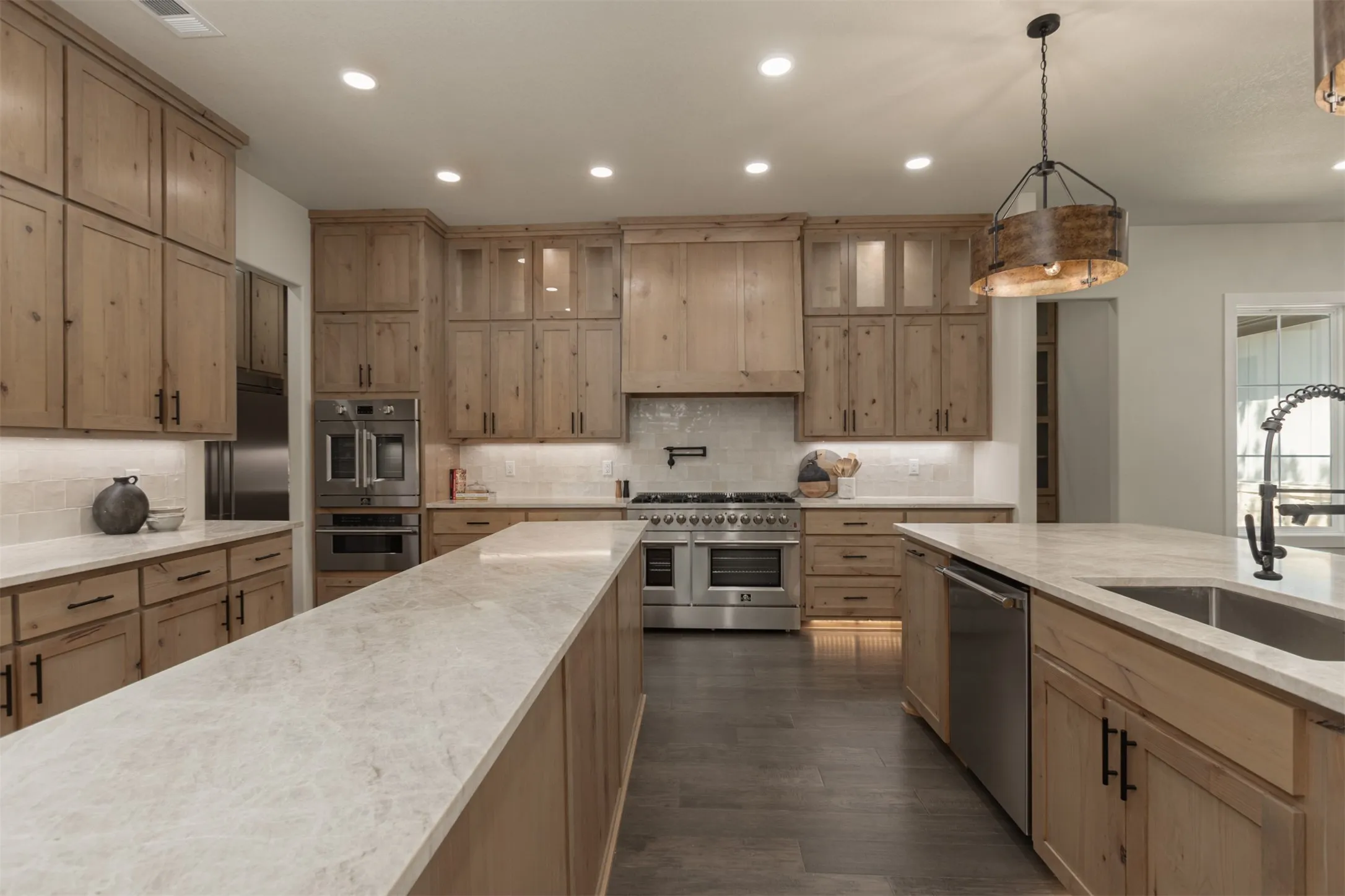 Expansive kitchen featuring light wood-finish cabinetry, light-toned countertops, integrated stainless steel appliances, a large center island, and wood-finish flooring