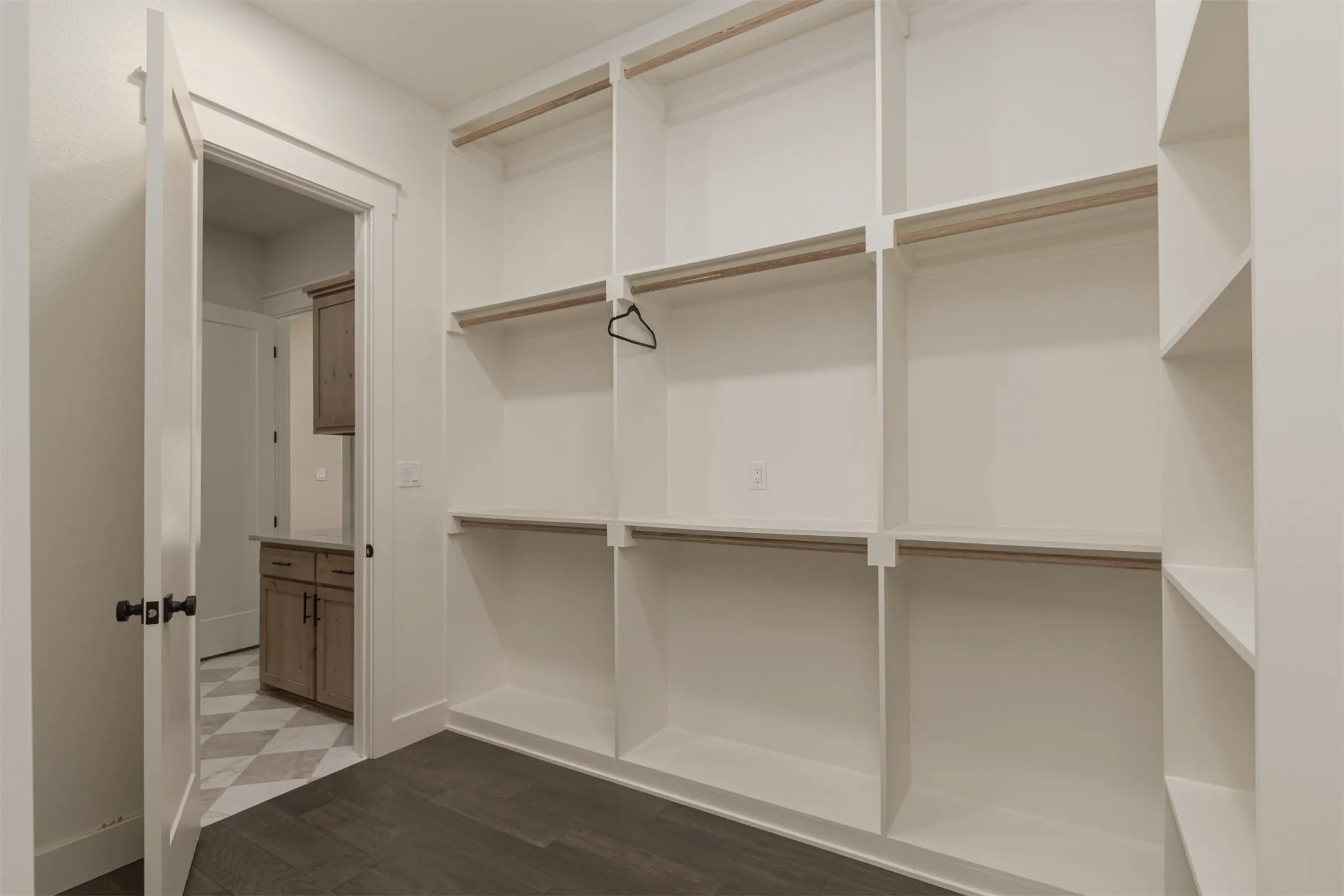 Integrated shelving and hanging rods, wood-finish flooring, and a paneled interior door with dark hardware