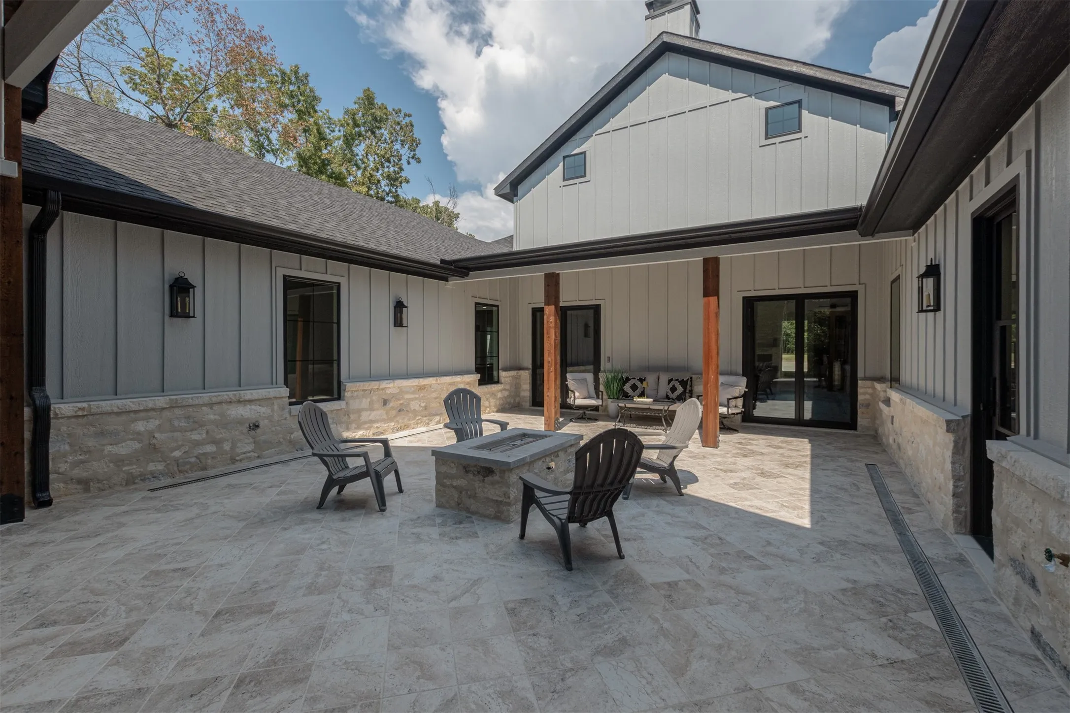 Expansive outdoor patio with stone tile flooring, a built-in fire pit, and wood support beams