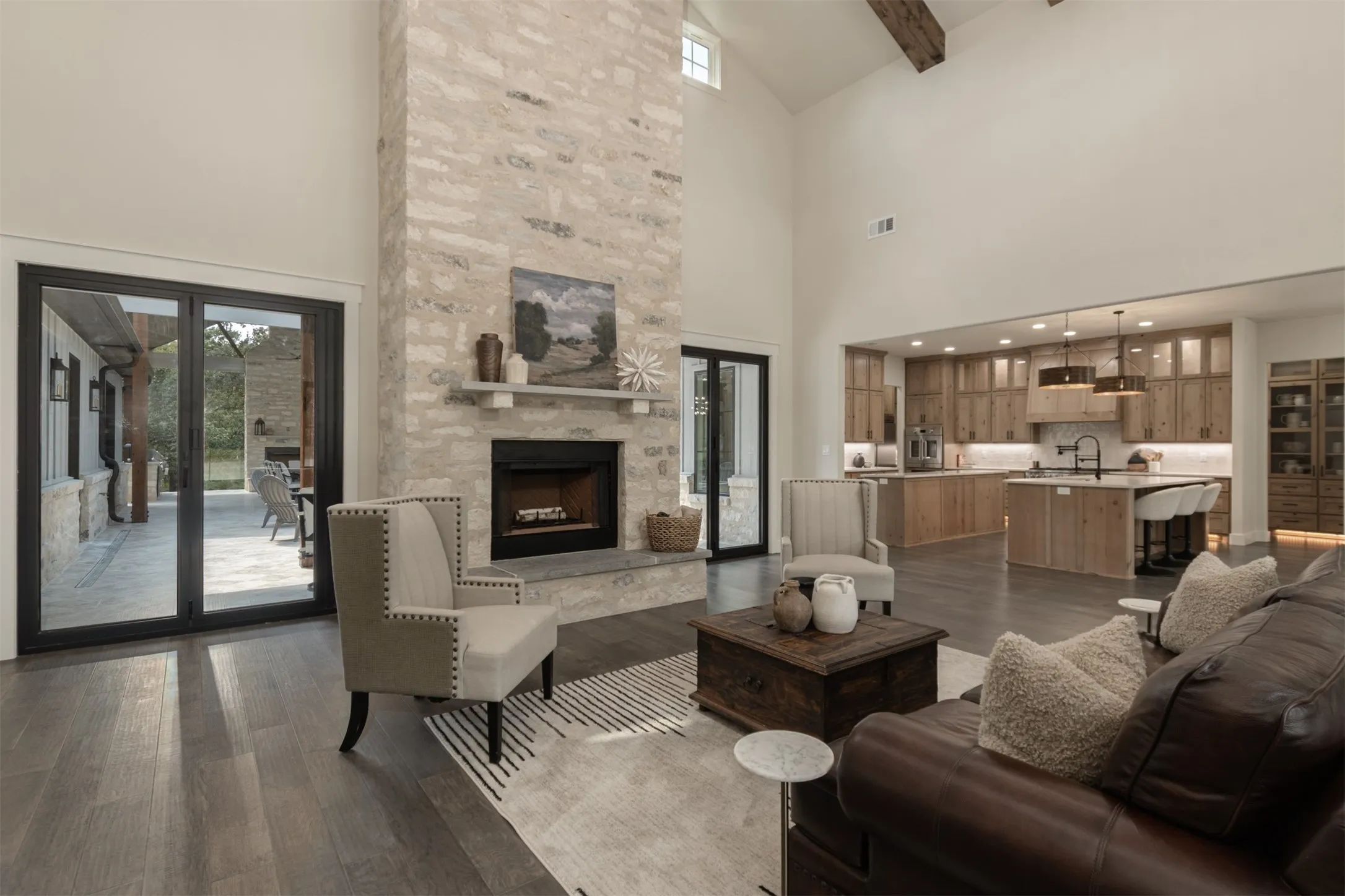 Vaulted ceiling with exposed wood beams, stone fireplace, wood-finish flooring, two-tone kitchen cabinetry, and built-in kitchen island seating