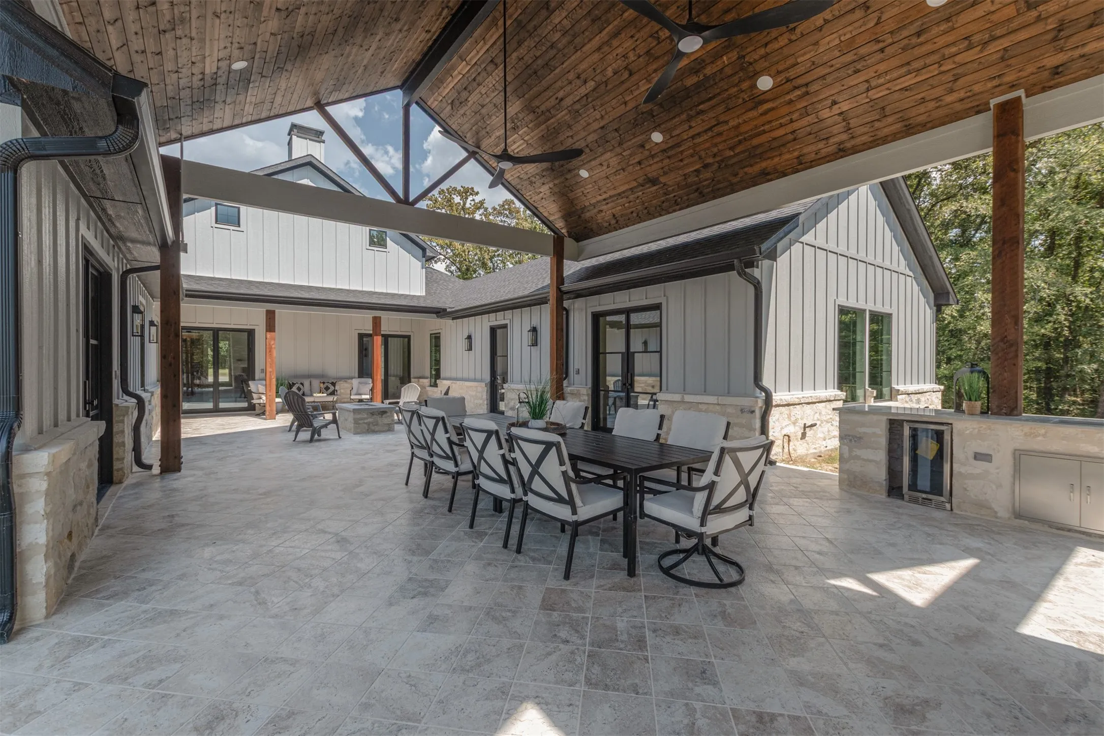 Expansive outdoor patio featuring a vaulted wood-finish ceiling, integrated outdoor kitchen with stainless steel appliances, a built-in fire pit, and large format tile flooring