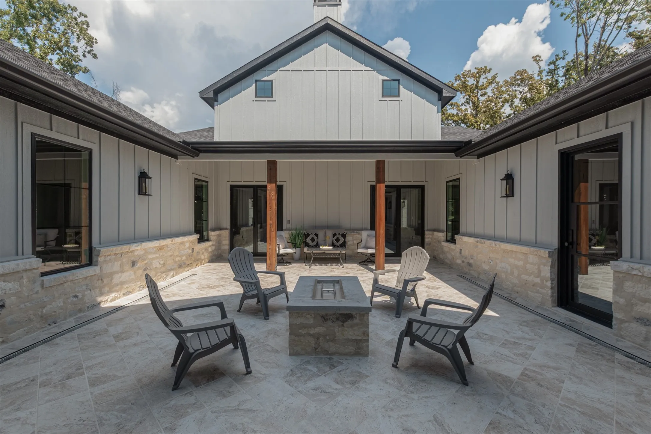 U-shaped patio with tiled flooring, stone base walls, black-framed windows, and an integrated fire pit