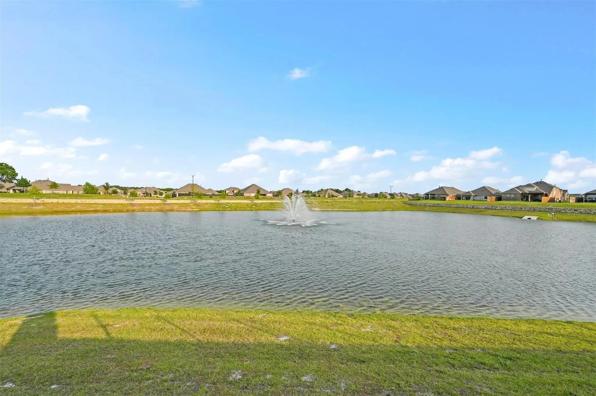 Waterfront property featuring a pond with an active fountain and a grassy bank