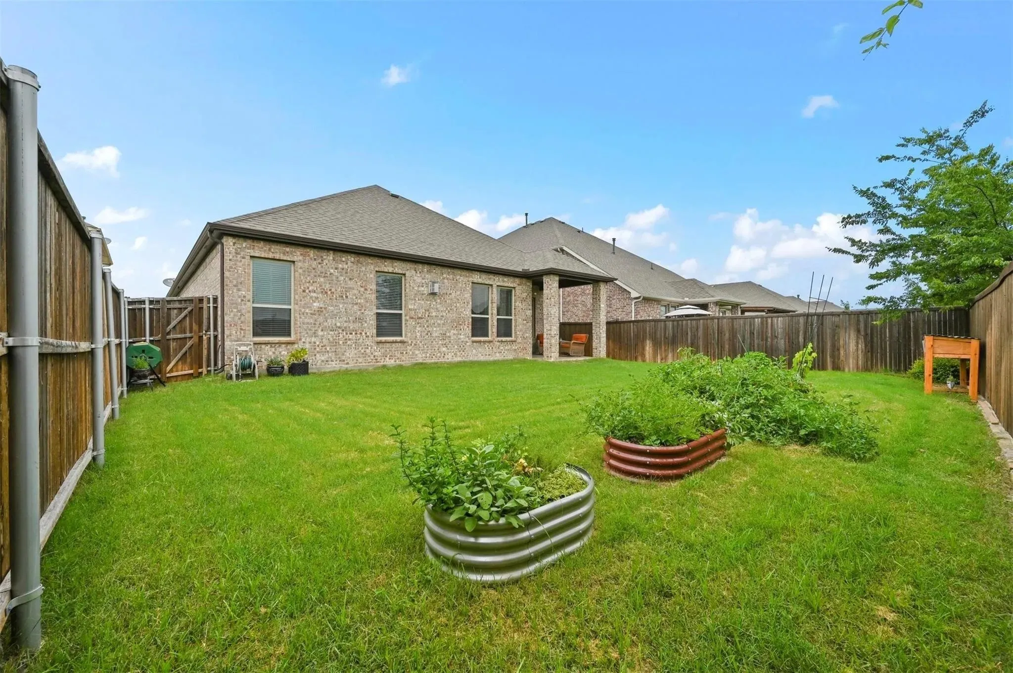 Expansive backyard featuring a manicured lawn, full privacy fencing, and raised garden beds