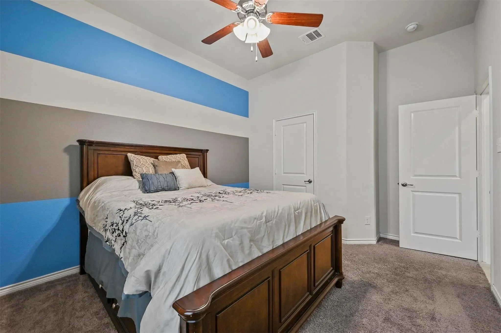 Carpeted room featuring a ceiling fan with wood-finish blades, two panel doors, and a wall with a decorative stripe design