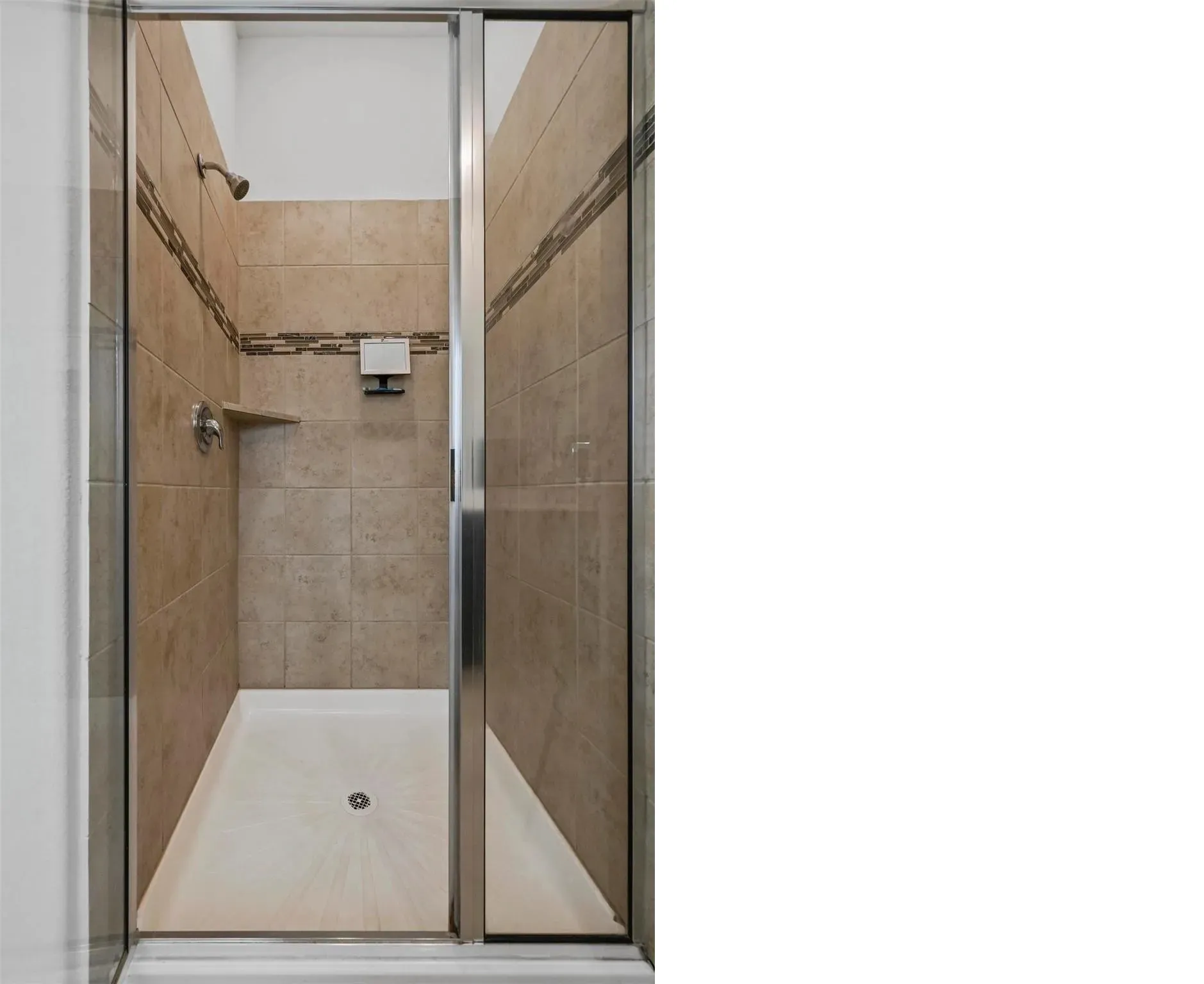 Tiled shower with a mosaic accent band, built-in corner shelf, and glass enclosure