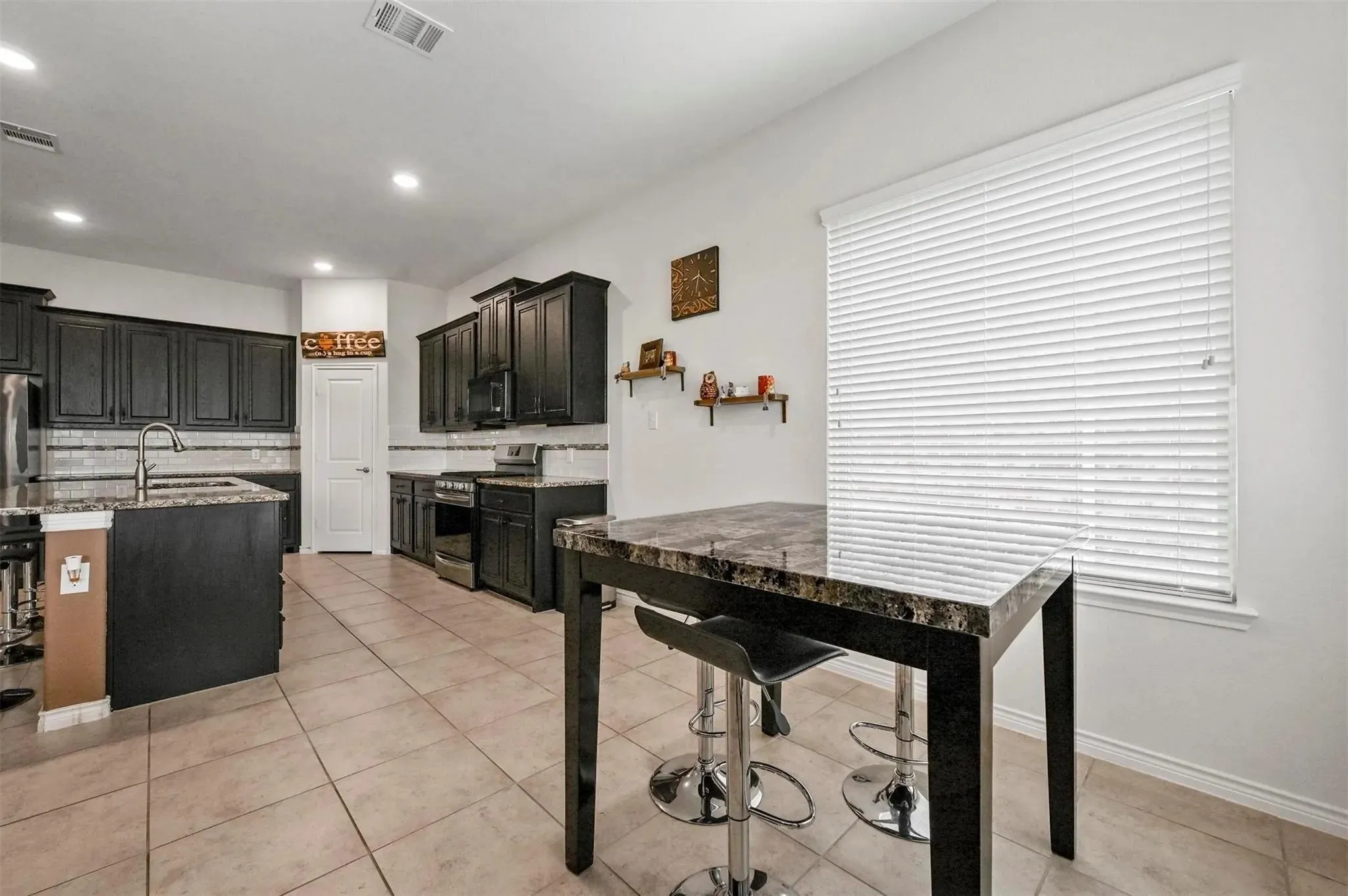 Kitchen featuring dark wood cabinetry, stainless steel appliances, a tile backsplash, and stone-finish countertops