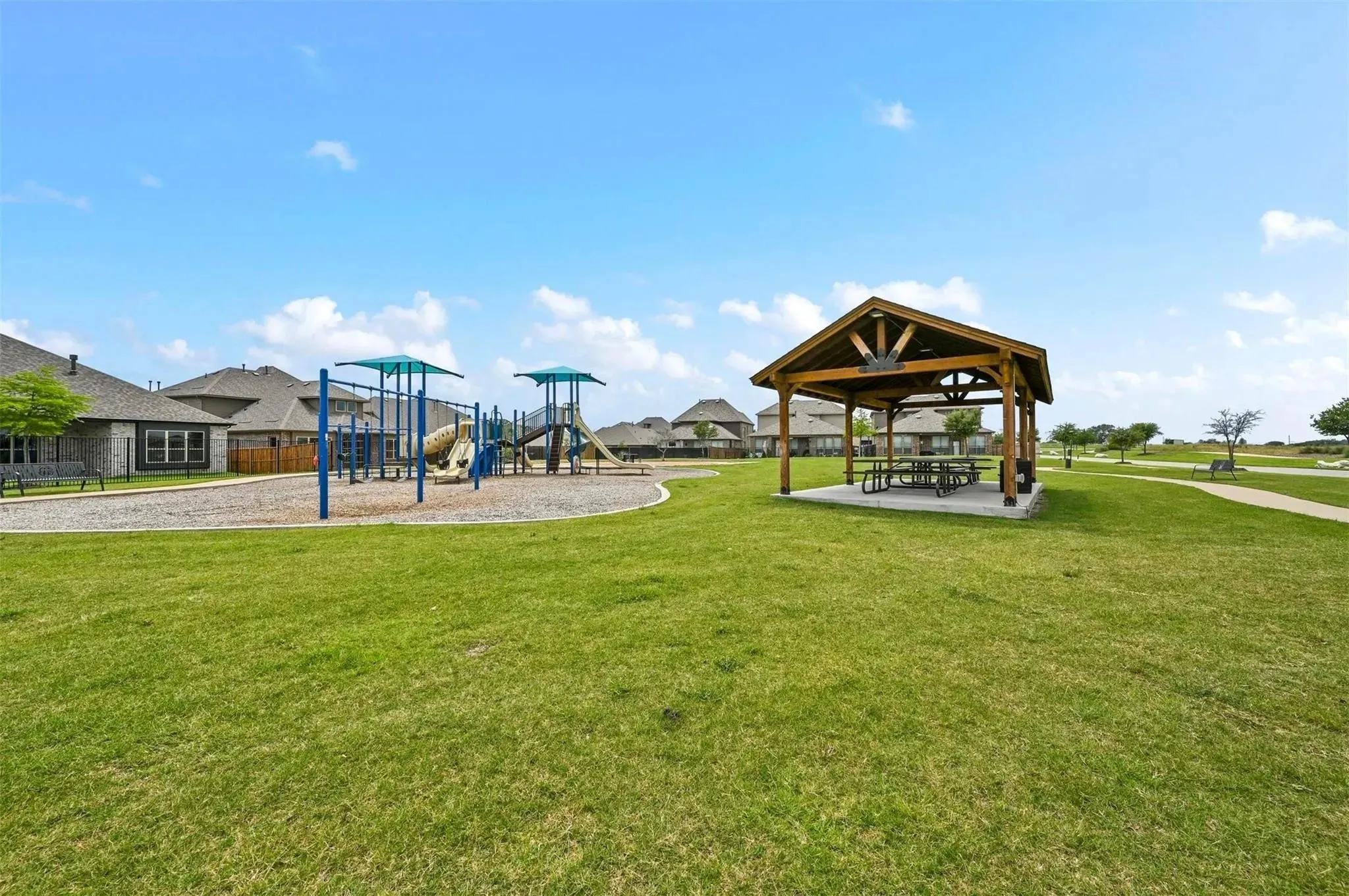 Expansive green space featuring a playground structure, a covered picnic area, and paved walking paths