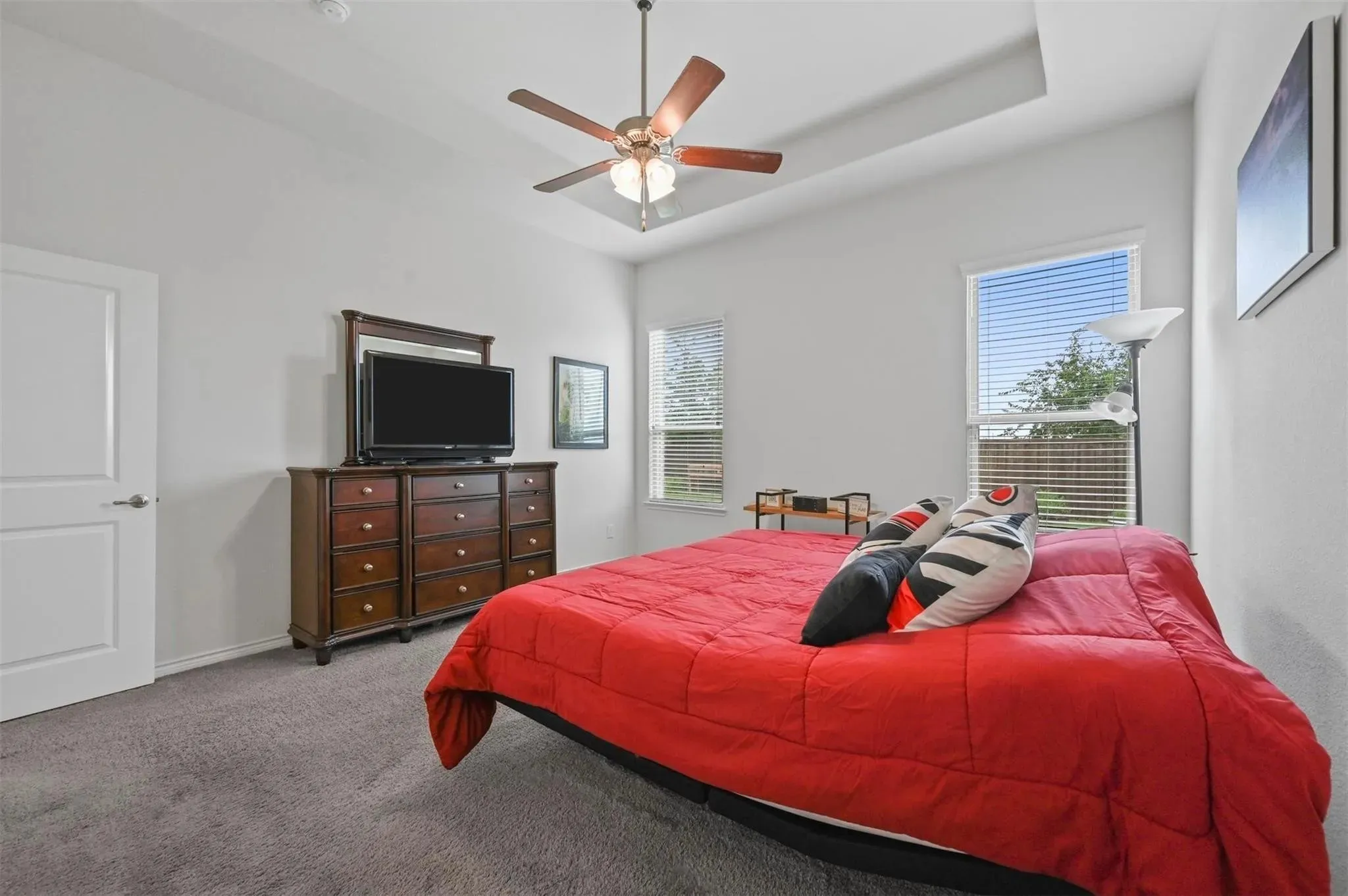 Tray ceiling with a ceiling fan, two windows with blinds, and neutral carpeting
