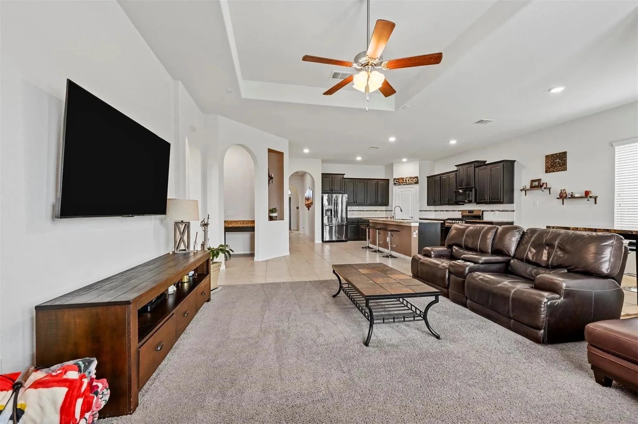 Tray ceiling with a ceiling fan, recessed lighting, arched doorways, and tile flooring