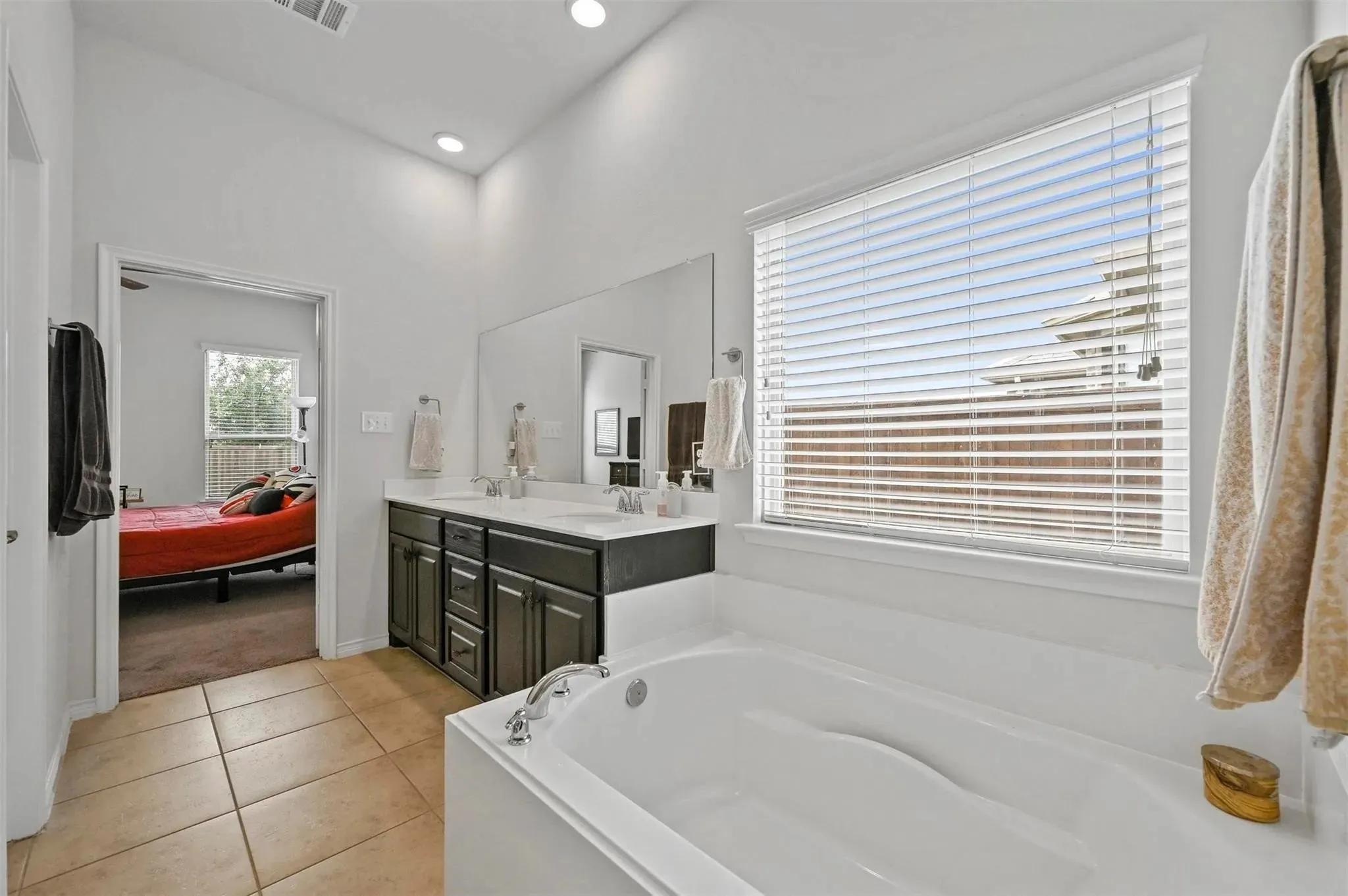 Soaking tub with tile surround, dual vanity with undermount sinks, large wall-mounted mirror, and recessed lighting