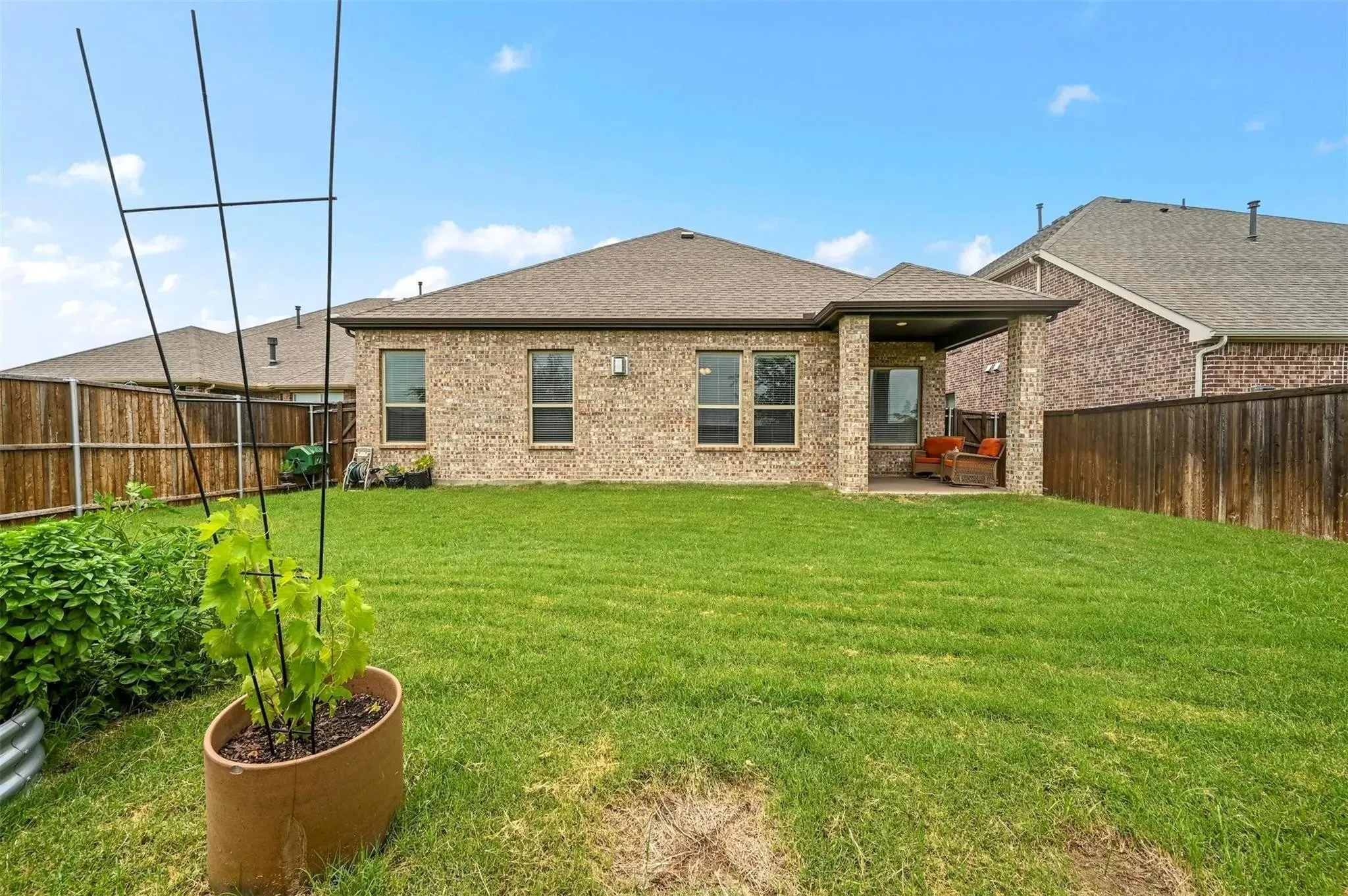 Expansive backyard with a manicured lawn, full brick exterior, covered patio, and privacy fencing